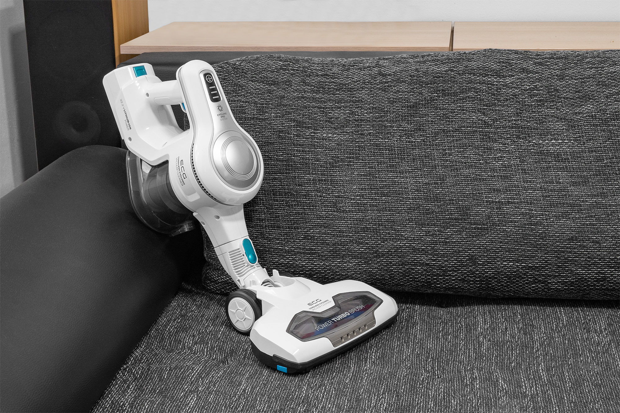 Weiß-silberner kabelloser Staubsauger auf einem grauen Sofa.