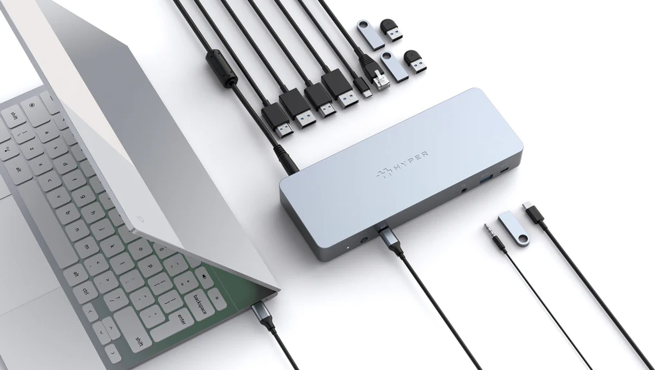 Portátil con hub USB y dispositivos conectados. Cables y memorias USB sobre superficie blanca.