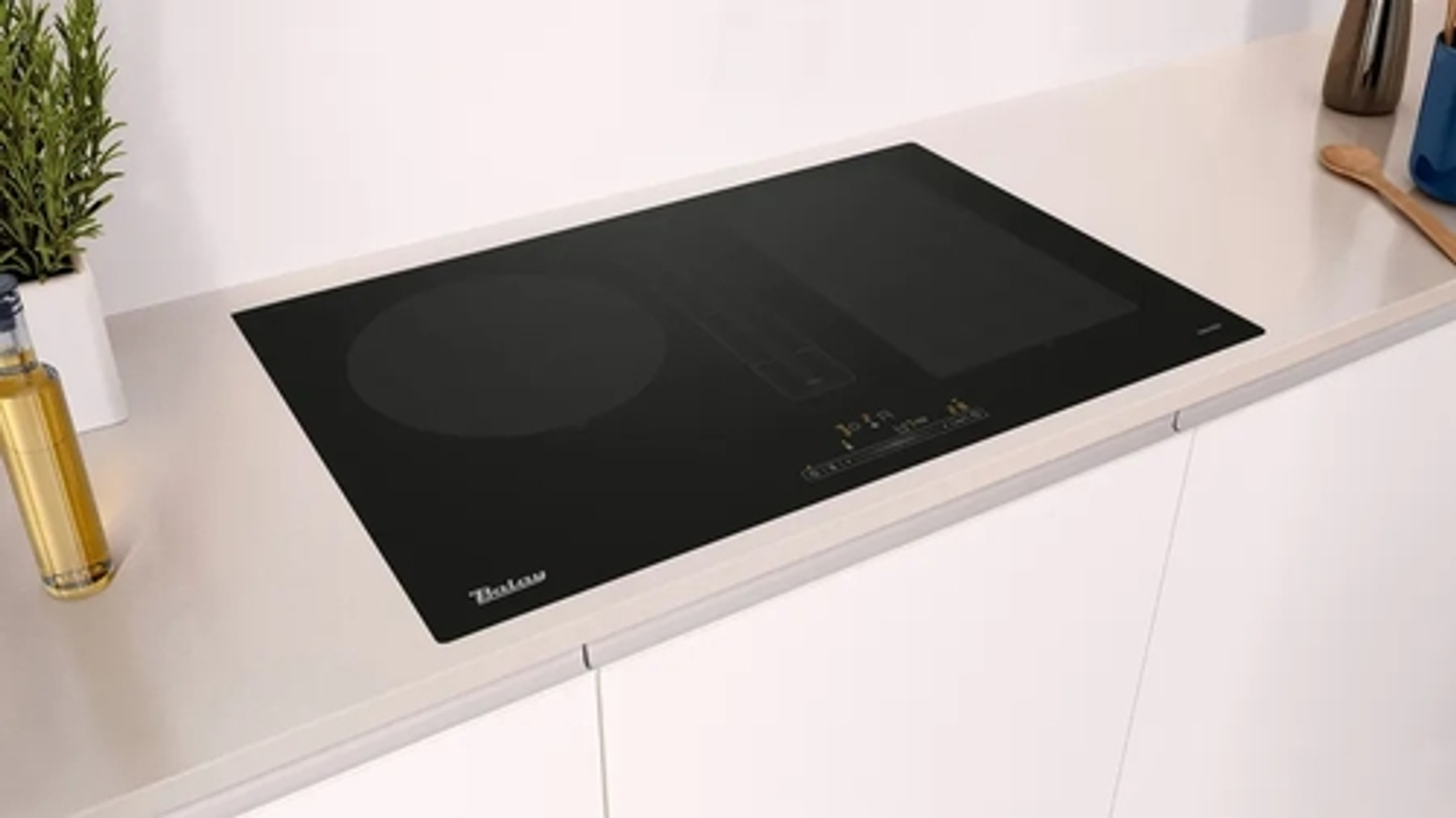 Czarna płyta indukcyjna na białym blacie, otoczenie kuchenne.