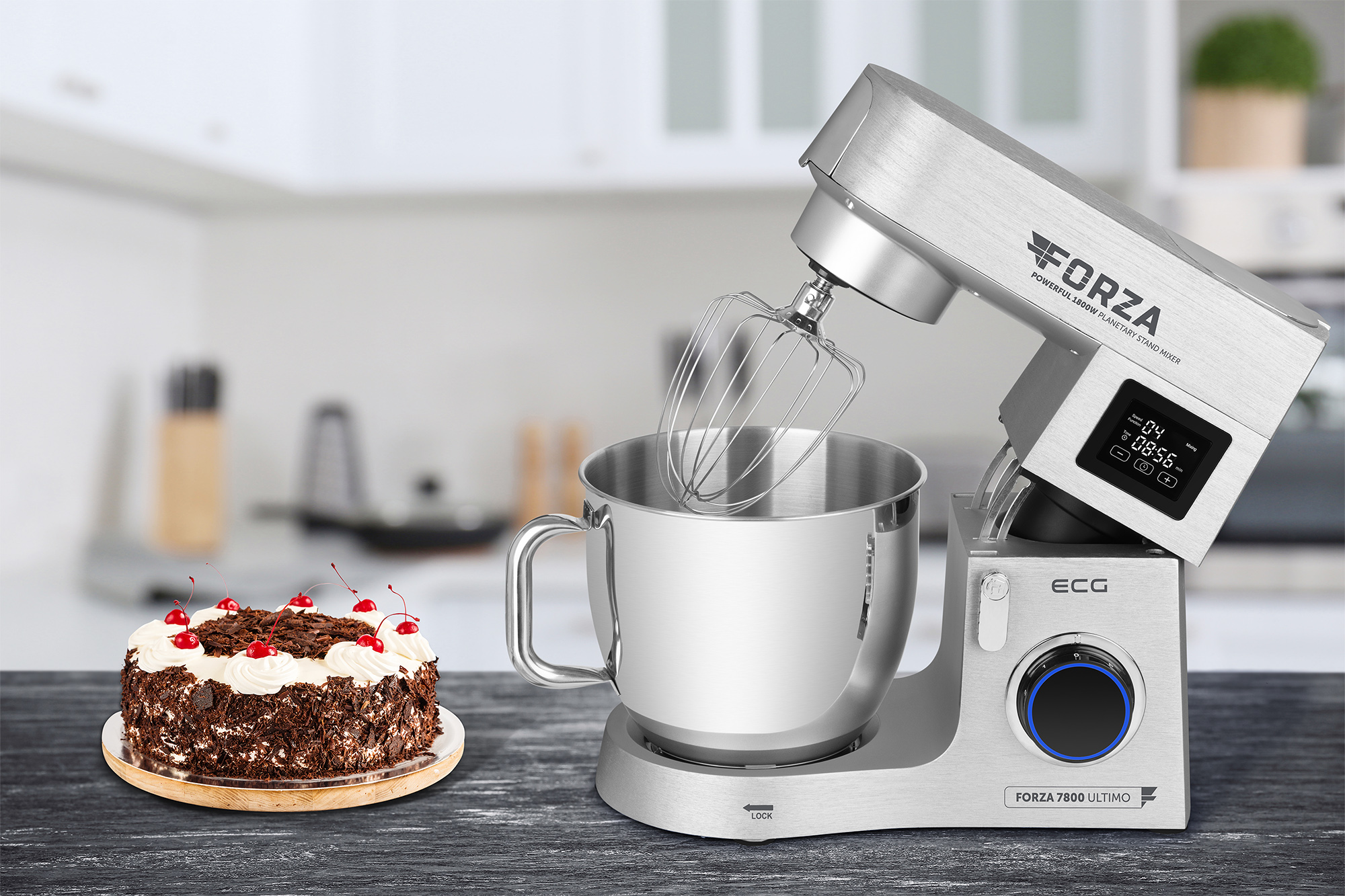 Eine Küchenmaschine mit einer Schüssel und Kuchen links. Die Küche ist im Hintergrund.