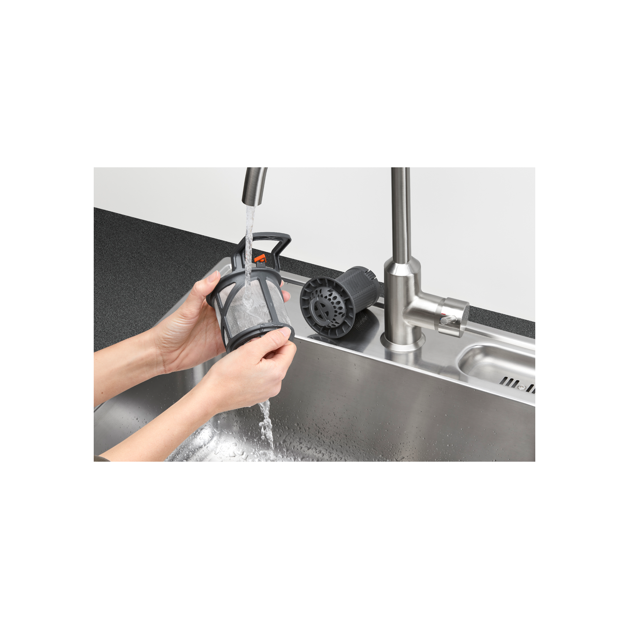 Dłonie płuczące filtr zmywarki pod bieżącą wodą w zlewozmywaku ze stali nierdzewnej.