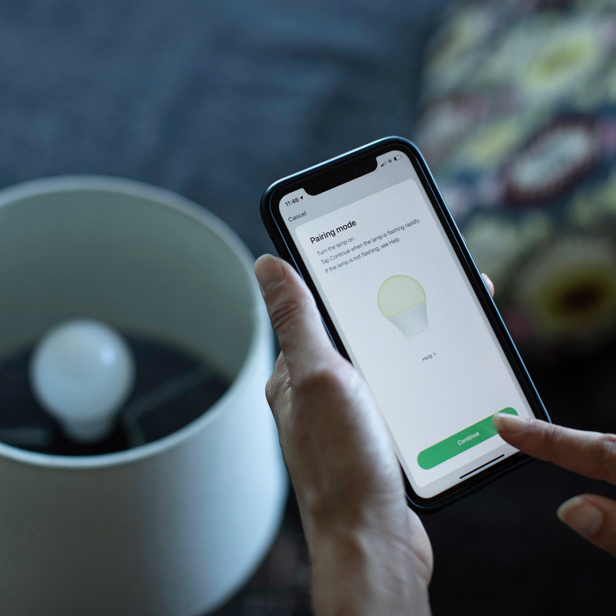 Eine Hand, die ein Smartphone im Pairing-Modus mit einer intelligenten Lampe hält und eine Lampe.