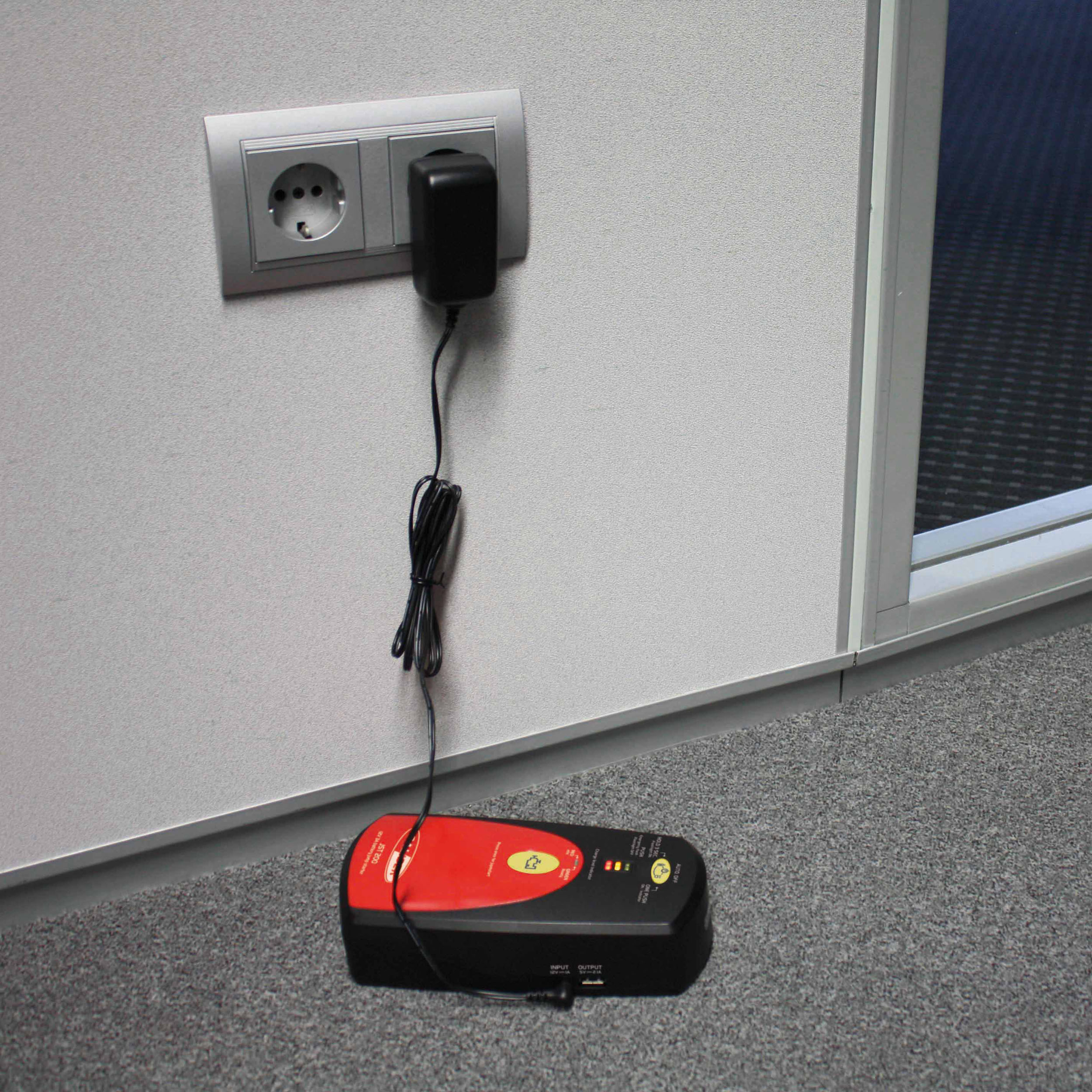 Ein Netzteil, das in eine Steckdose gesteckt ist, mit einer schwarzen Box, die über ein Kabel mit dem Boden verbunden ist.