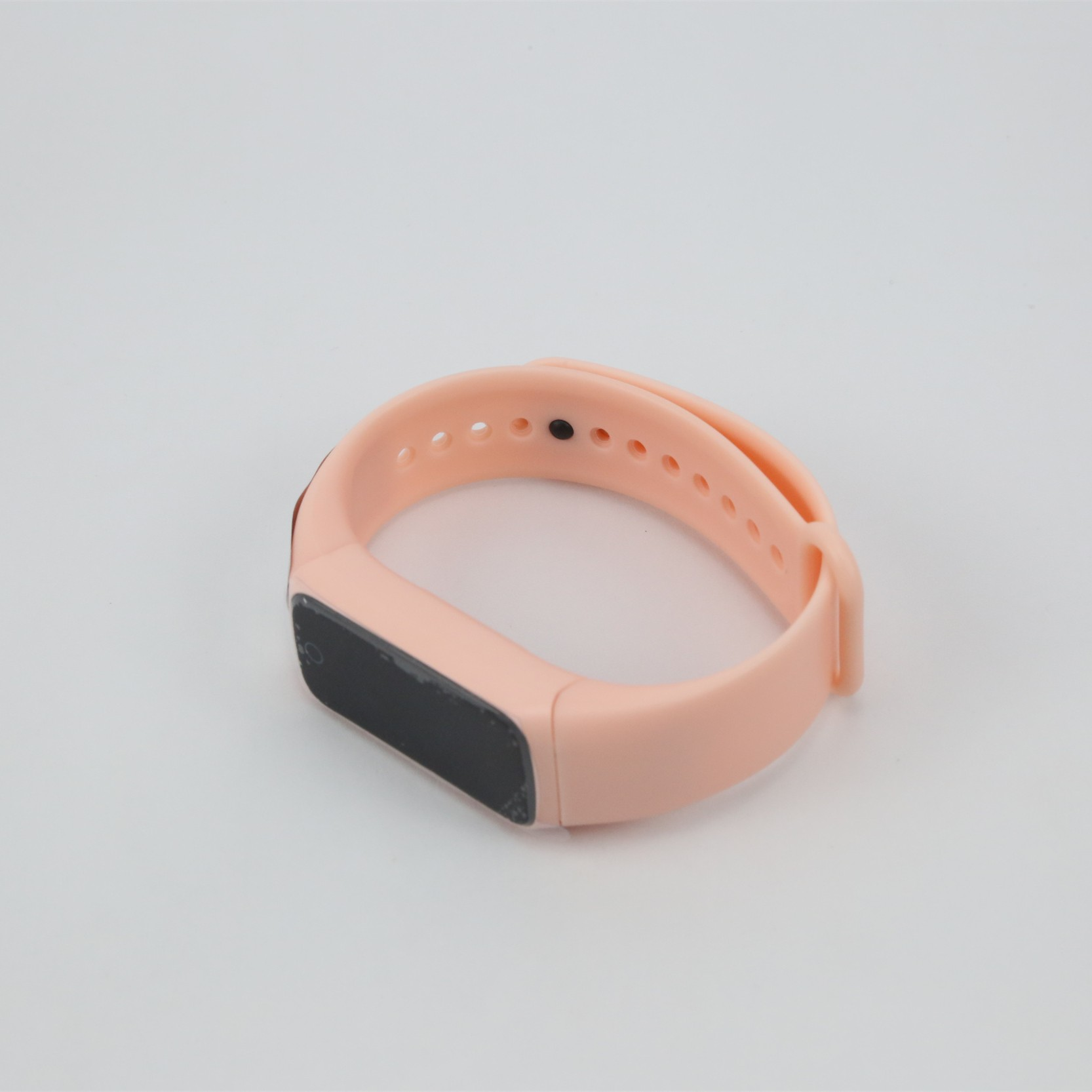 Różowy zegarek fitness, leżący na białej powierzchni.