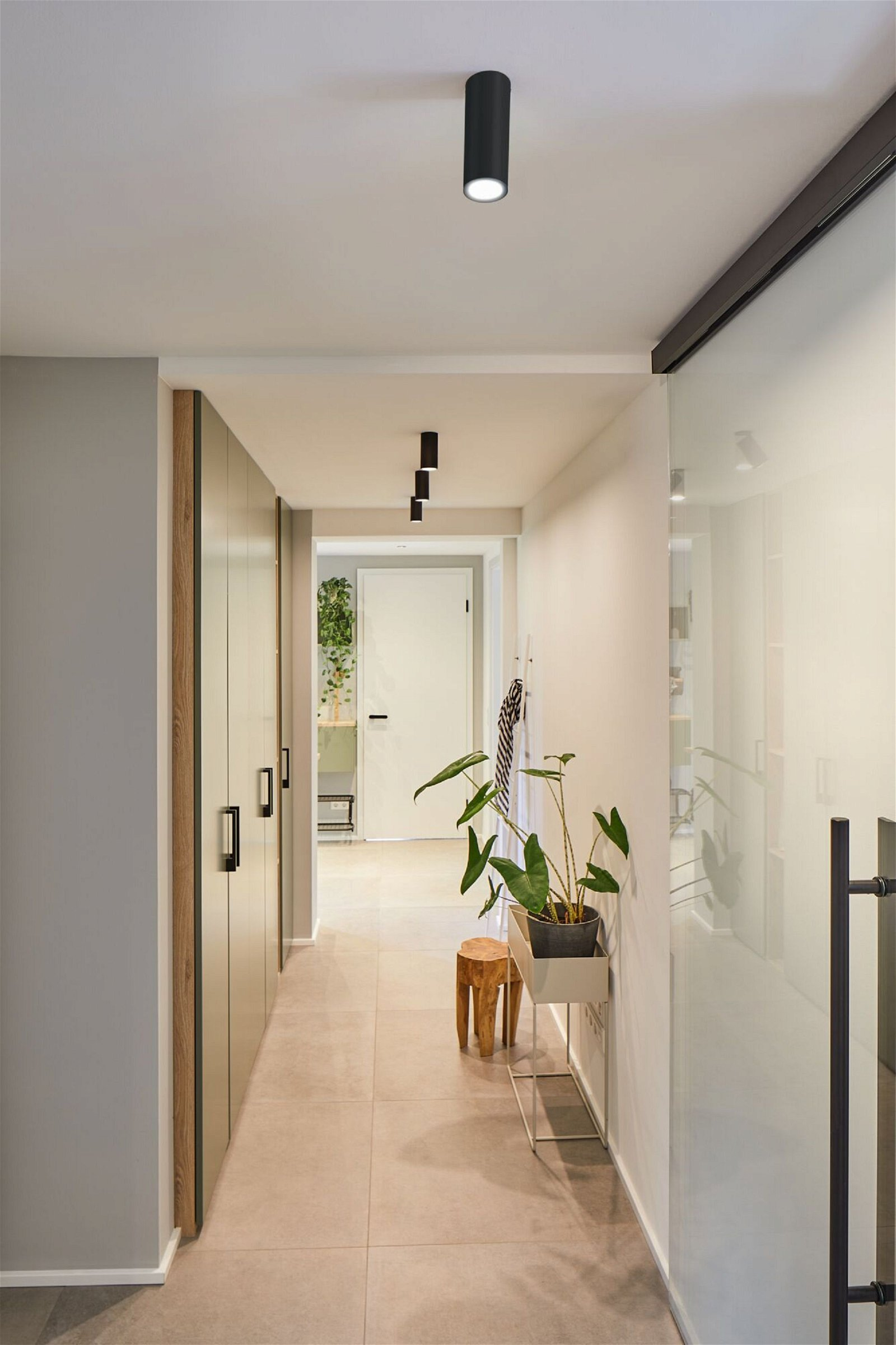 Korytarz z oprawą oświetleniową, rośliną i drewnianym stołkiem.