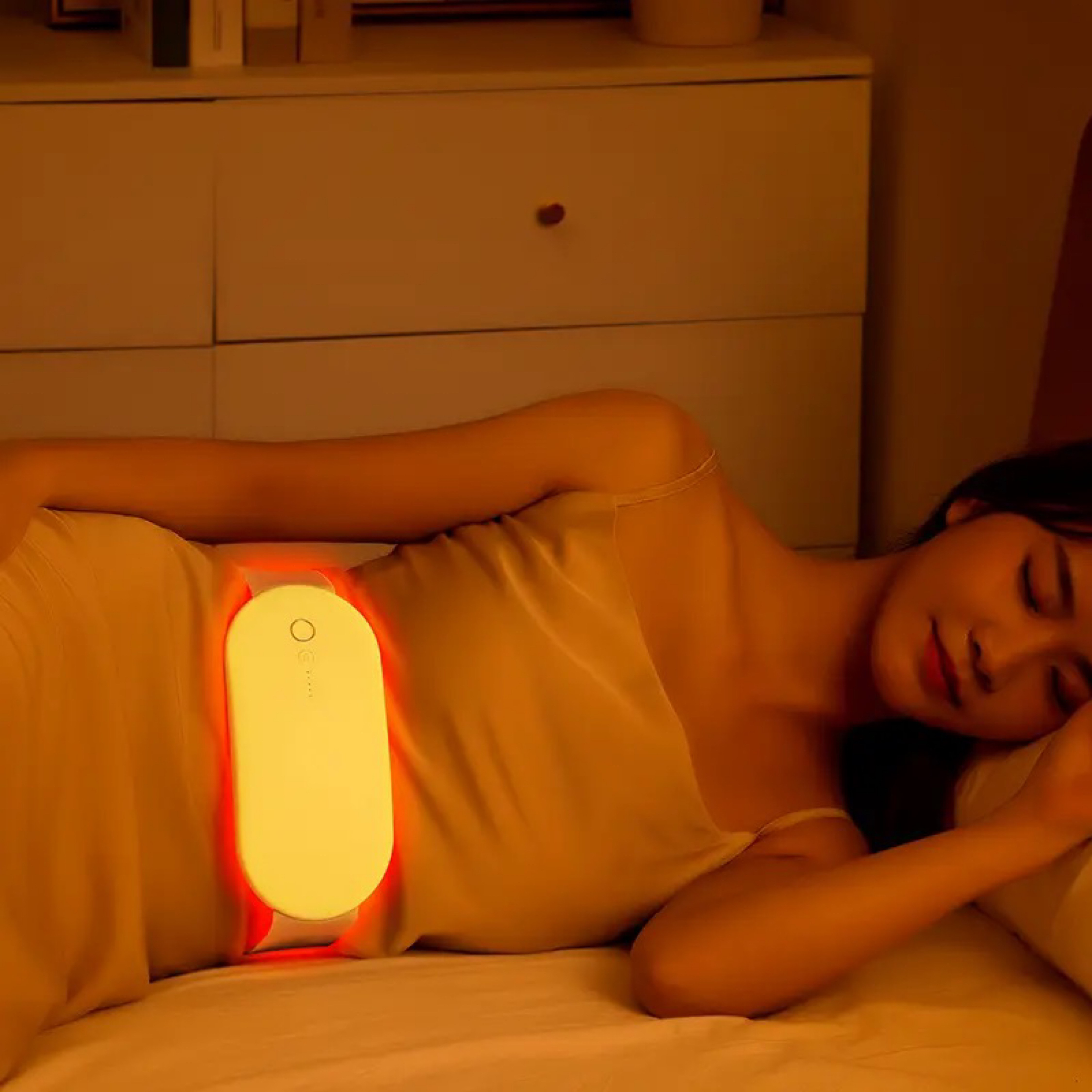 Kobieta leżąca w łóżku z poduszką rozgrzewającą na brzuchu, świecącą na czerwono.