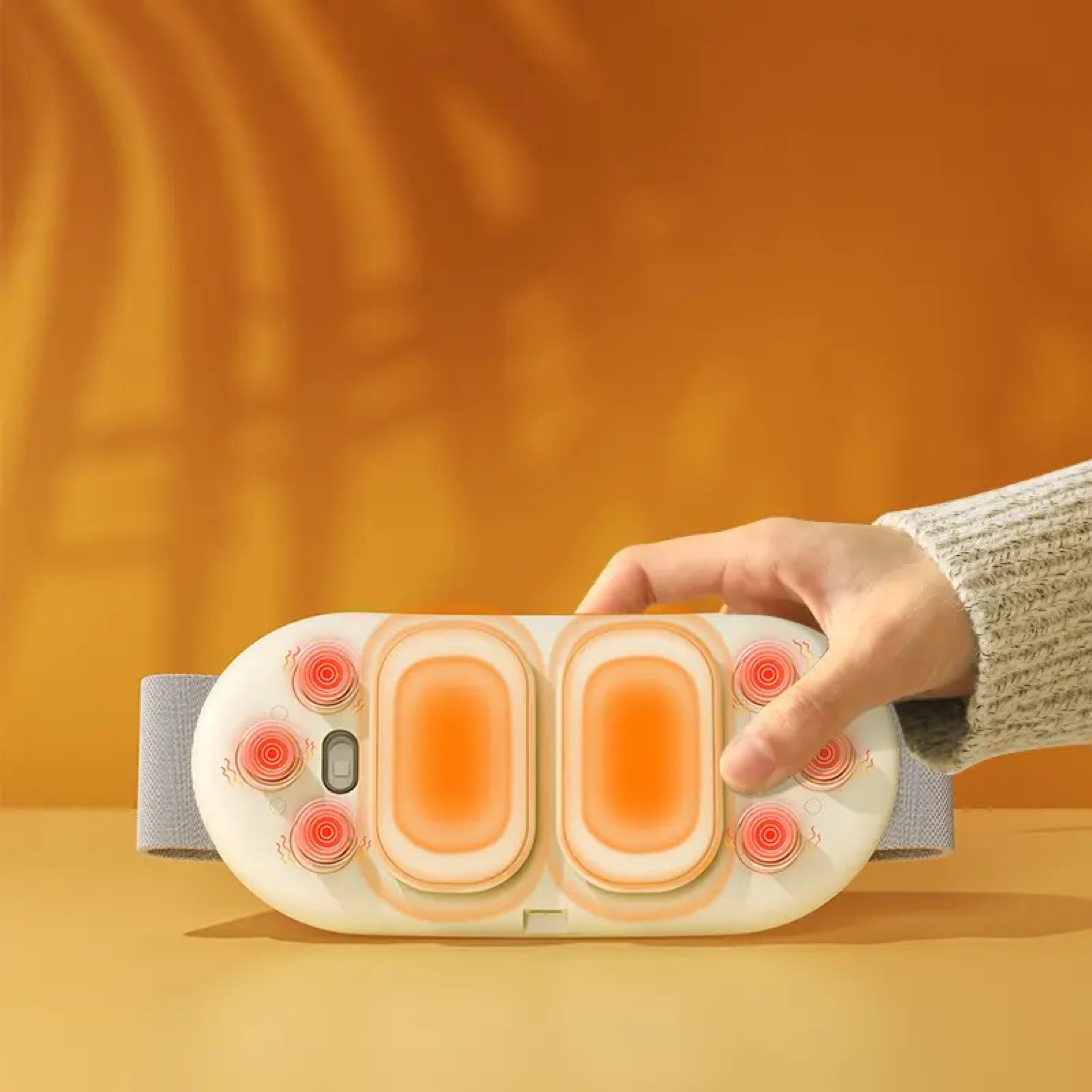 Dłoń trzymająca białe urządzenie do masażu z pomarańczowymi podkładkami grzewczymi i czerwonymi okręgami.