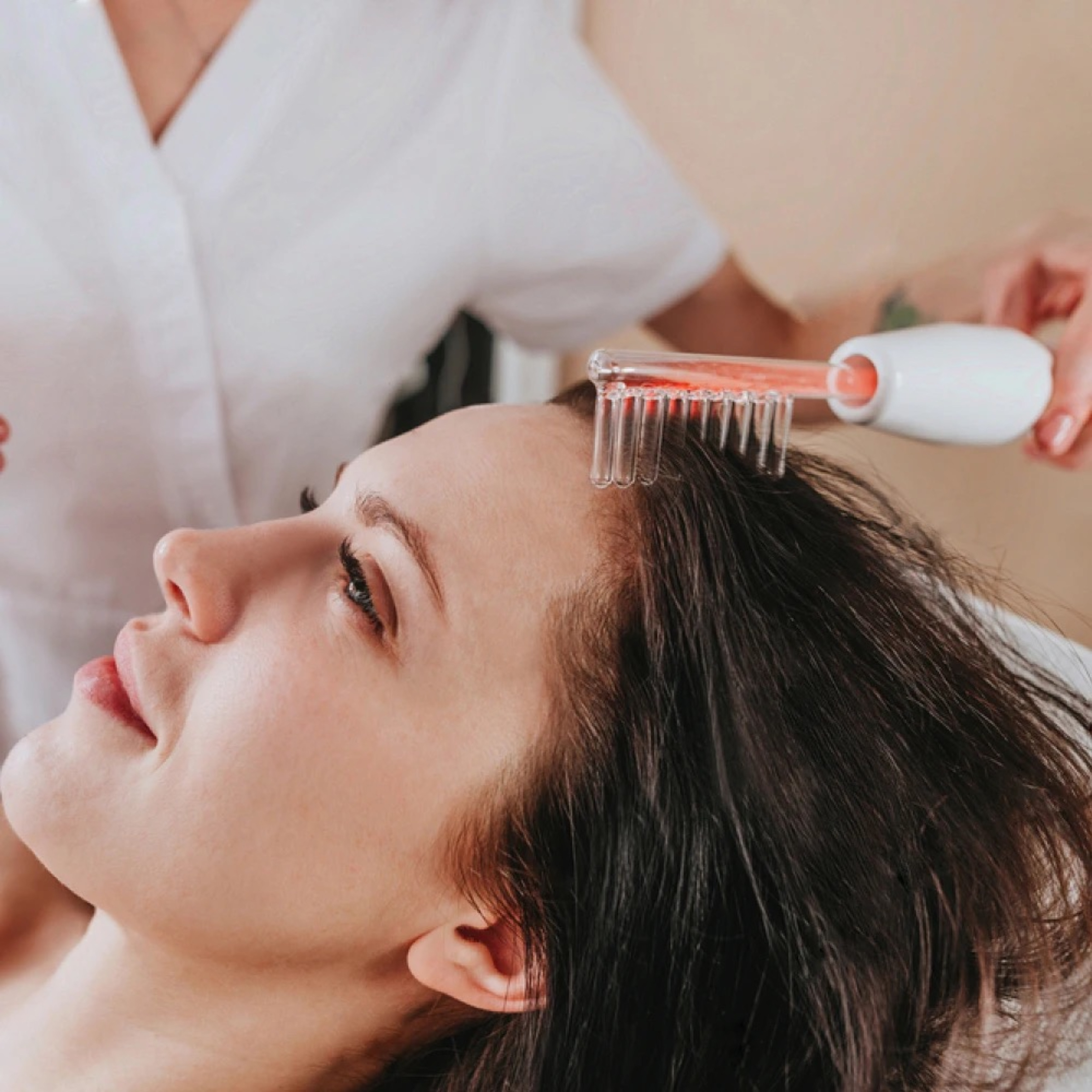 Kobieta otrzymująca zabieg na włosy z czerwonym urządzeniem w kształcie grzebienia, leżąc.