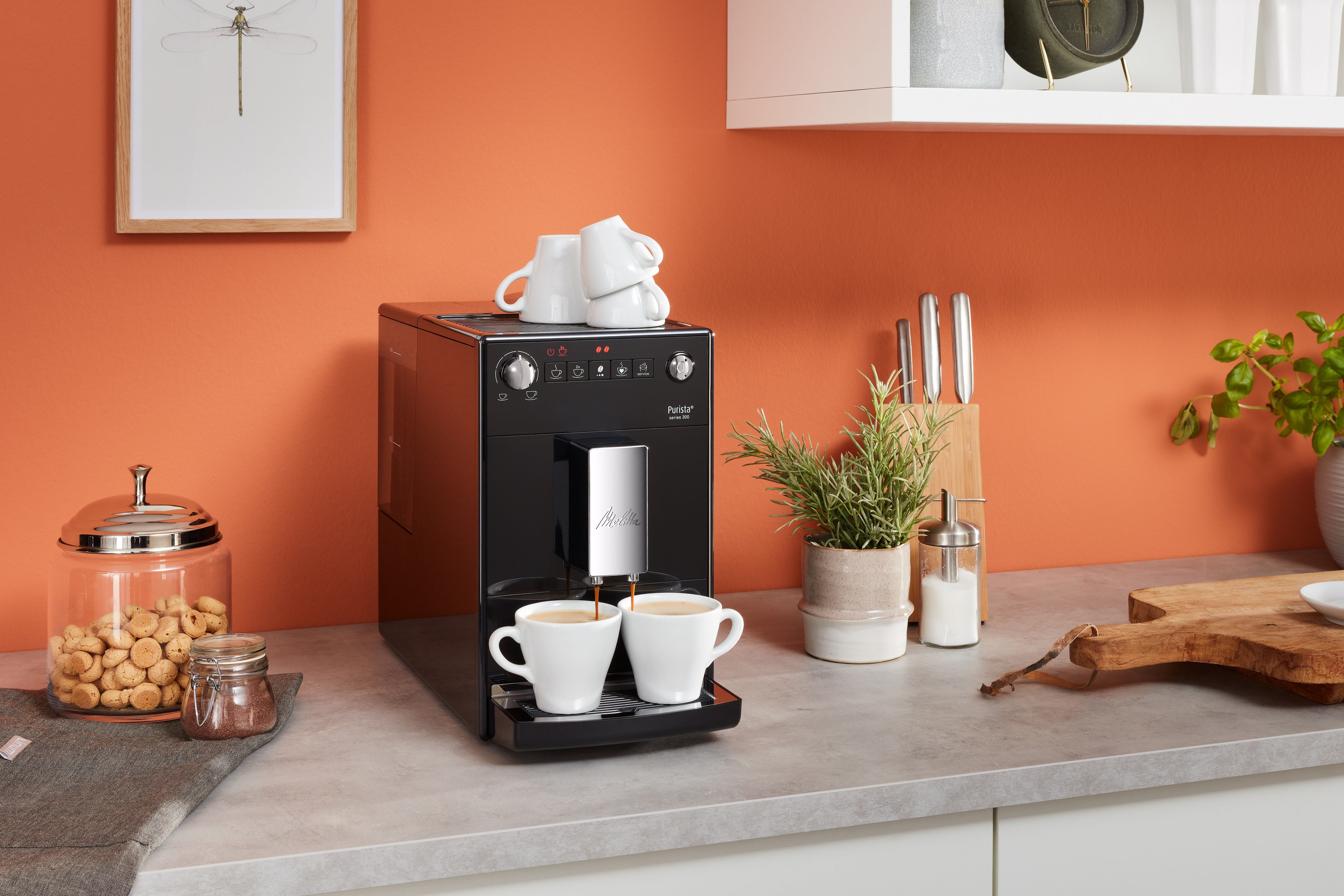 Eine schwarze Kaffeemaschine mit zwei gefüllten Tassen und gestapelten Tassen. Orange Wand.