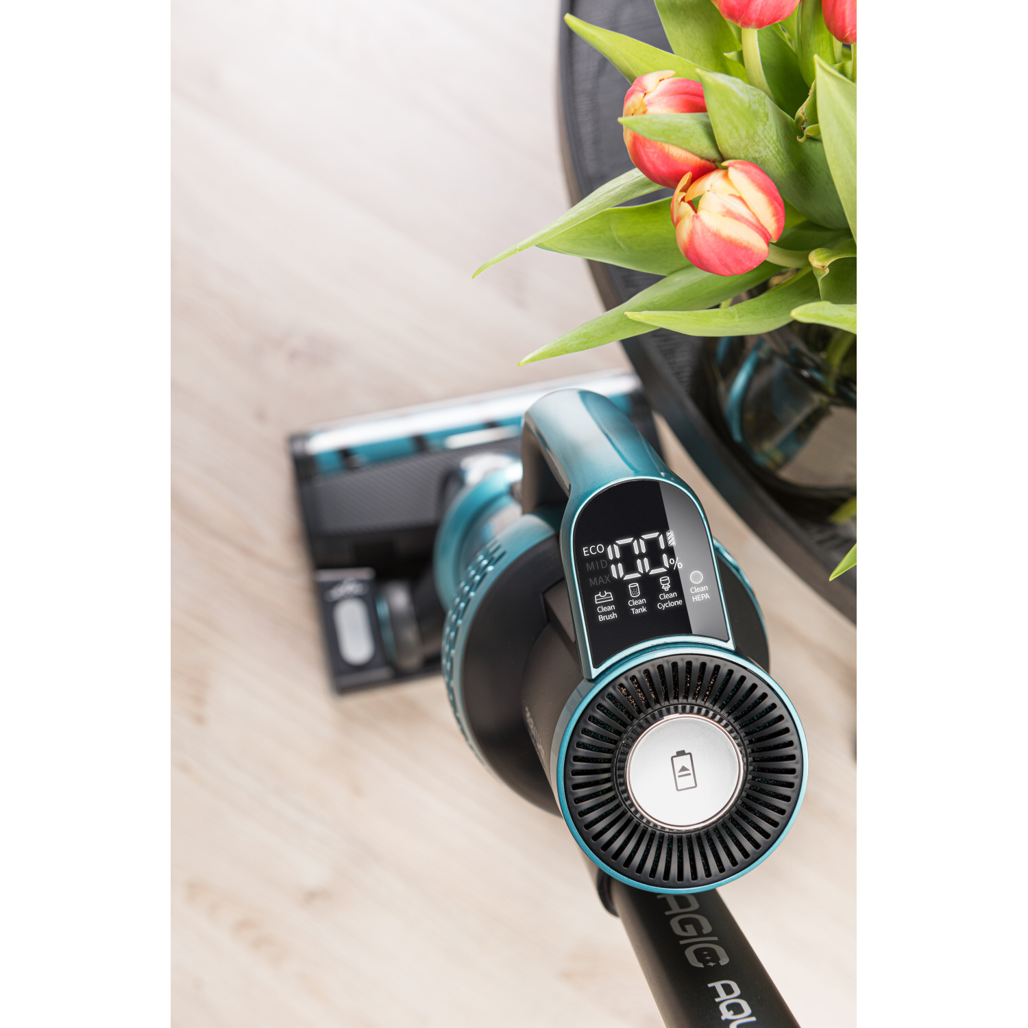 Türkis Staubsauger mit Digitalanzeige, Tulpen im Hintergrund, auf Holzfußboden.