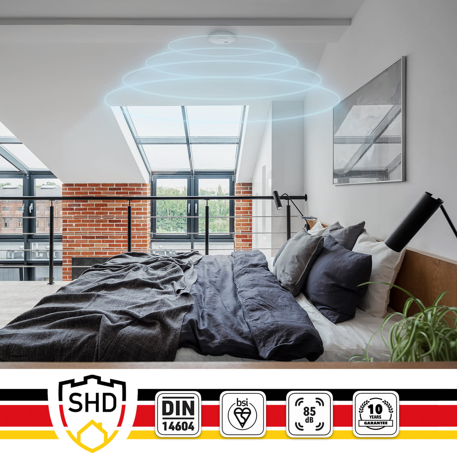 Ein Schlafzimmer mit Rauchmelder an der Decke, über einem Bett mit dunkelgrauer Bettwäsche.