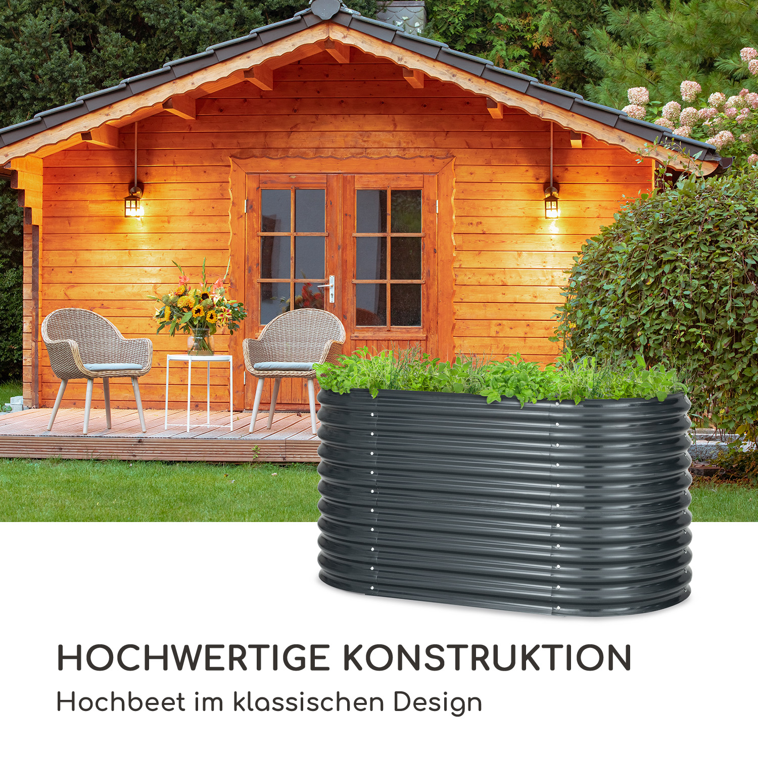 Ein schwarzes Hochbeet mit Grünzeug steht in einem Garten mit einem Holzhaus im Hintergrund.
