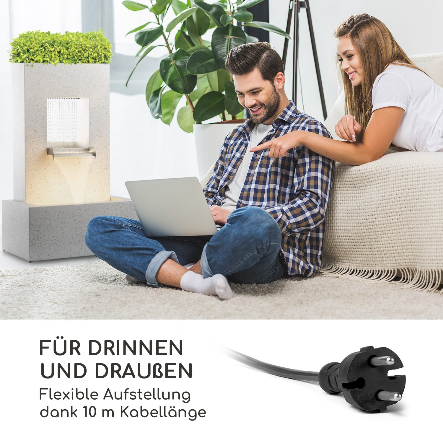 Paar an einem Brunnen, Mann mit Laptop und Netzkabel. Grüne Pflanzen.