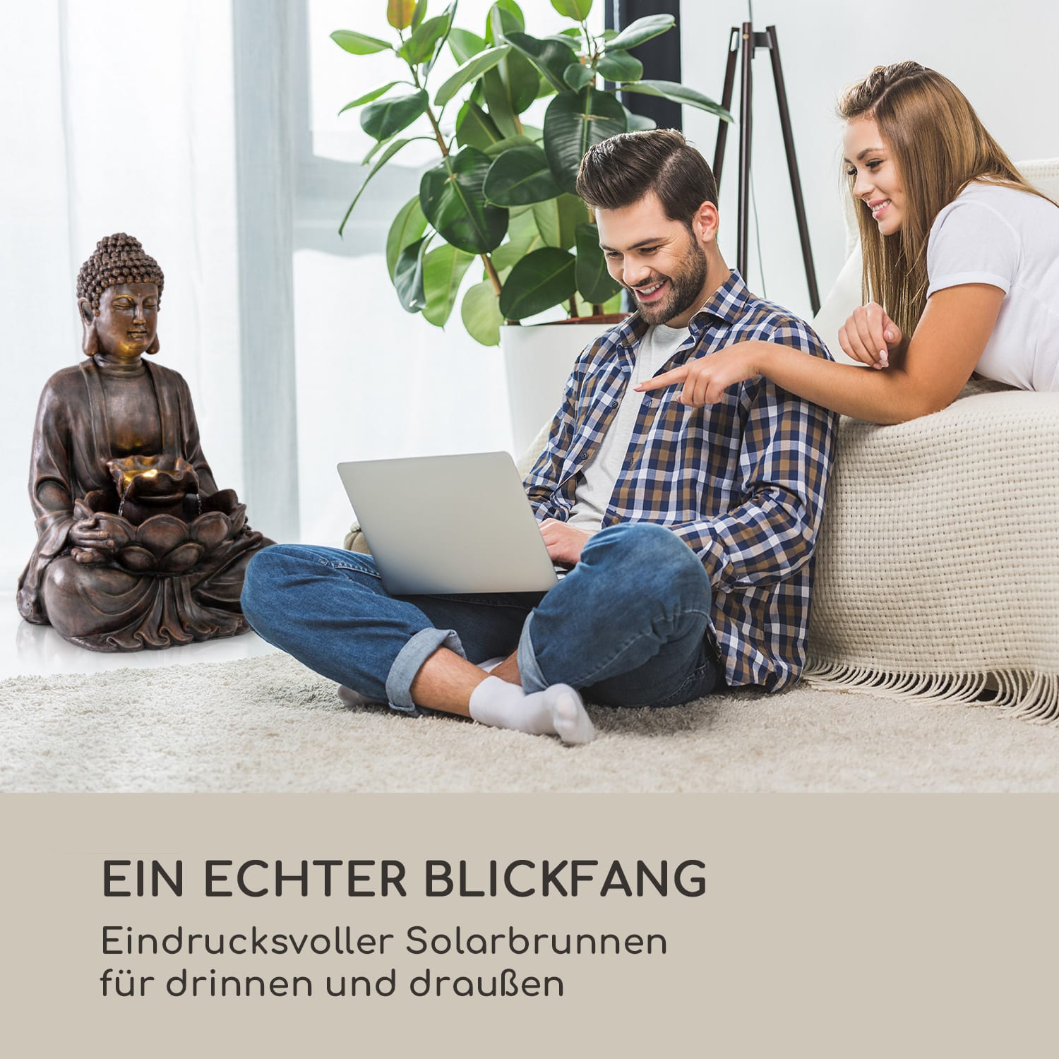 Ein Paar sitzt auf einem Sofa und schaut auf einen Laptop. Eine Buddha-Statue und eine Pflanze sind sichtbar.