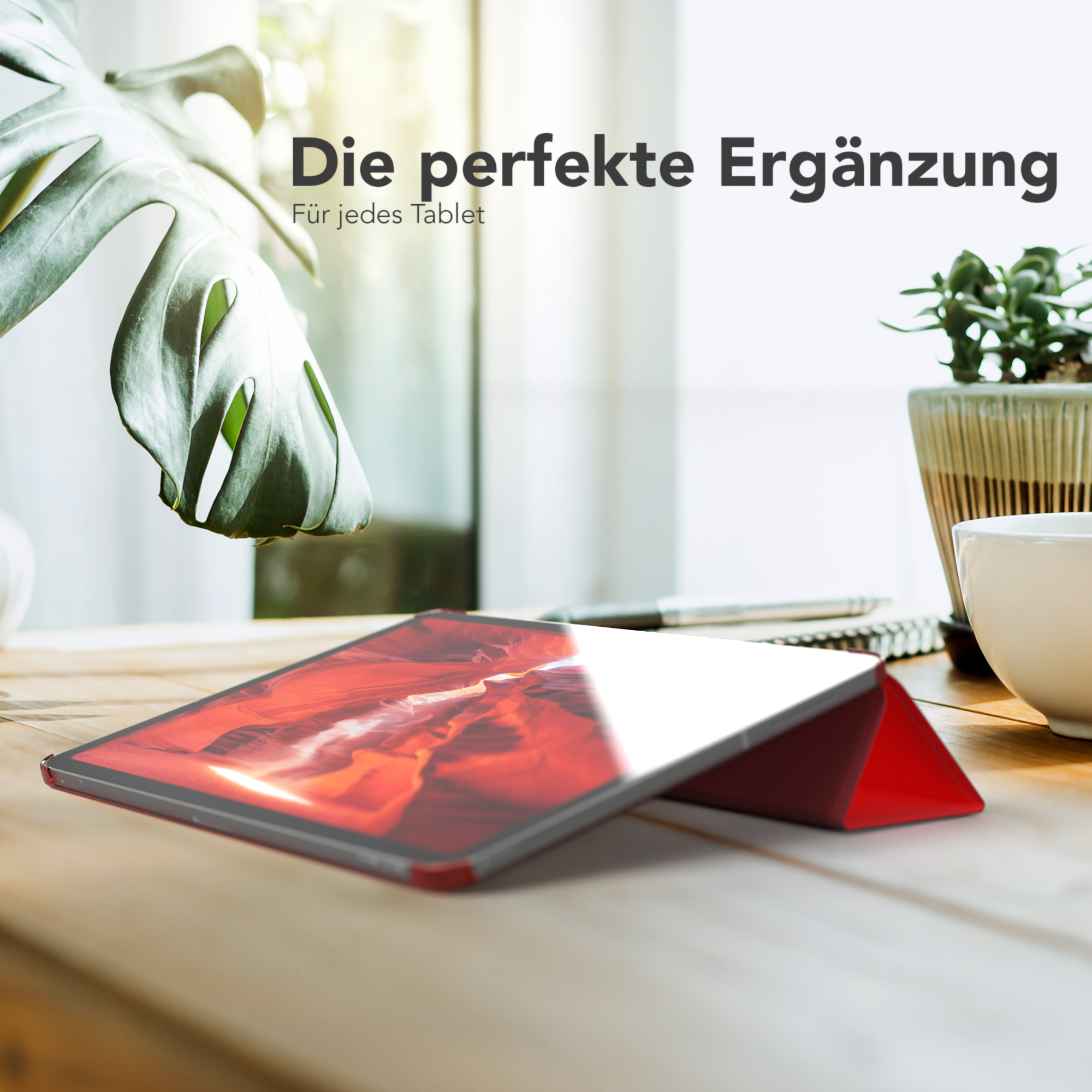 Ein Tablet in einem roten Gehäuse liegt auf einem Holztisch neben einer Pflanze und einer weißen Tasse.