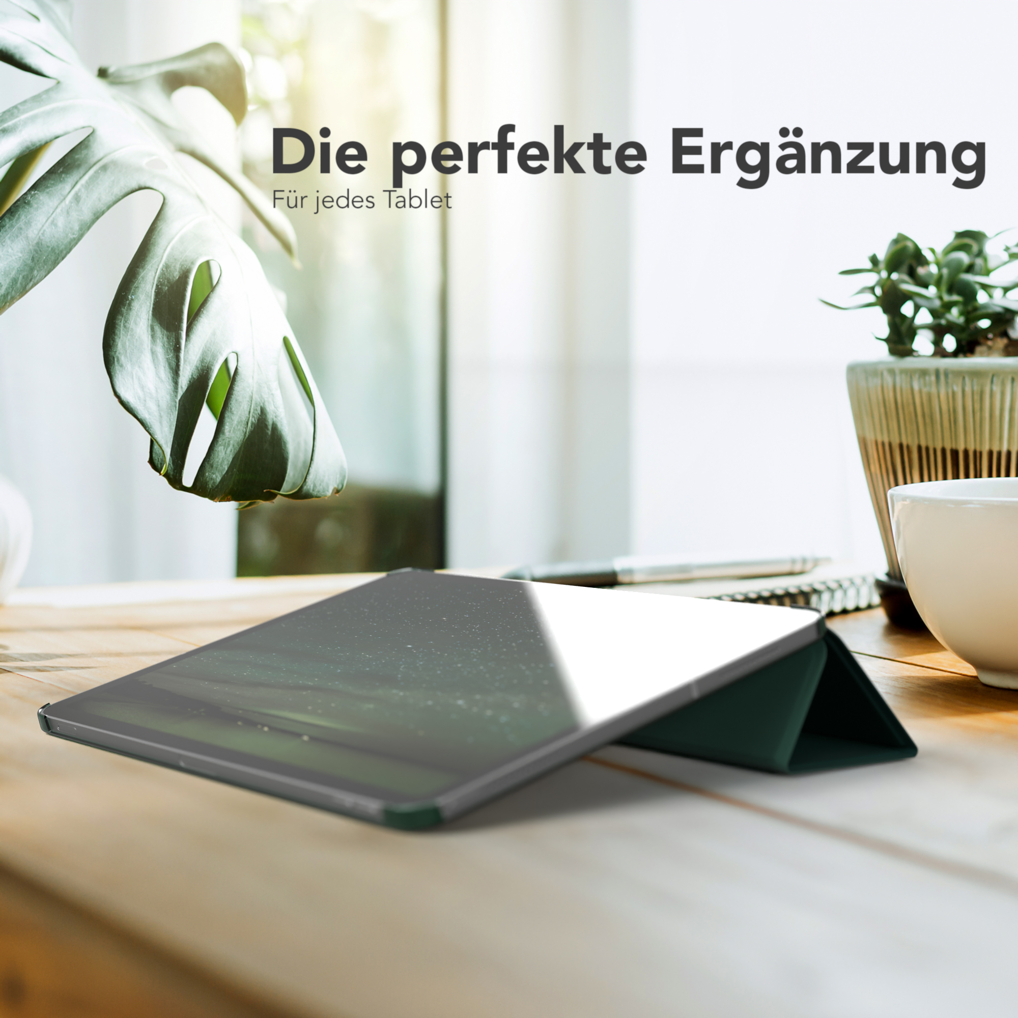Ein Tablet mit dunkelgrüner Hülle auf einem Holztisch mit einer Pflanze und einer Kaffeetasse im Hintergrund.