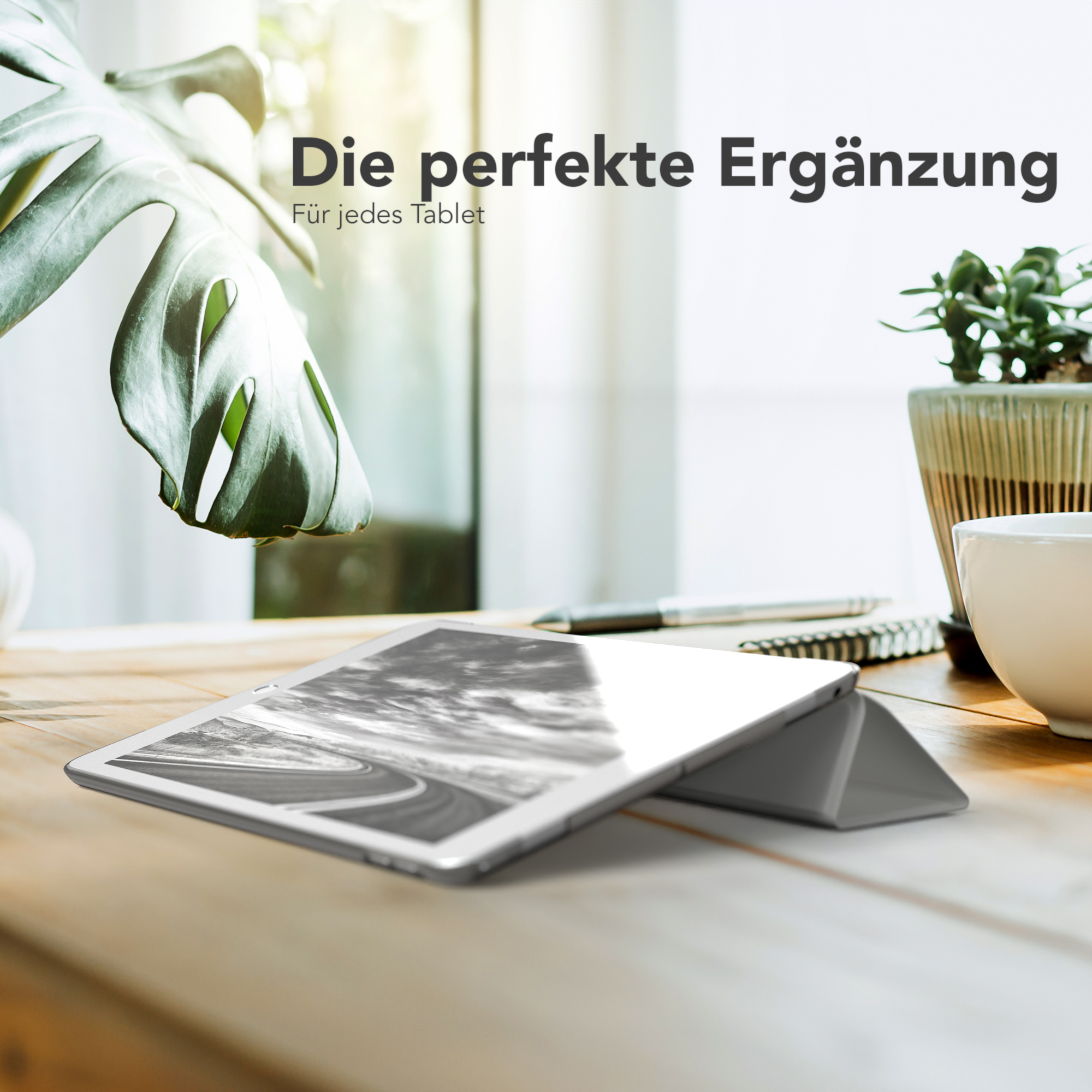 Ein iPad liegt auf einem Holztisch mit einem Blatt und einer Topfpflanze, beleuchtet von Sonnenlicht.