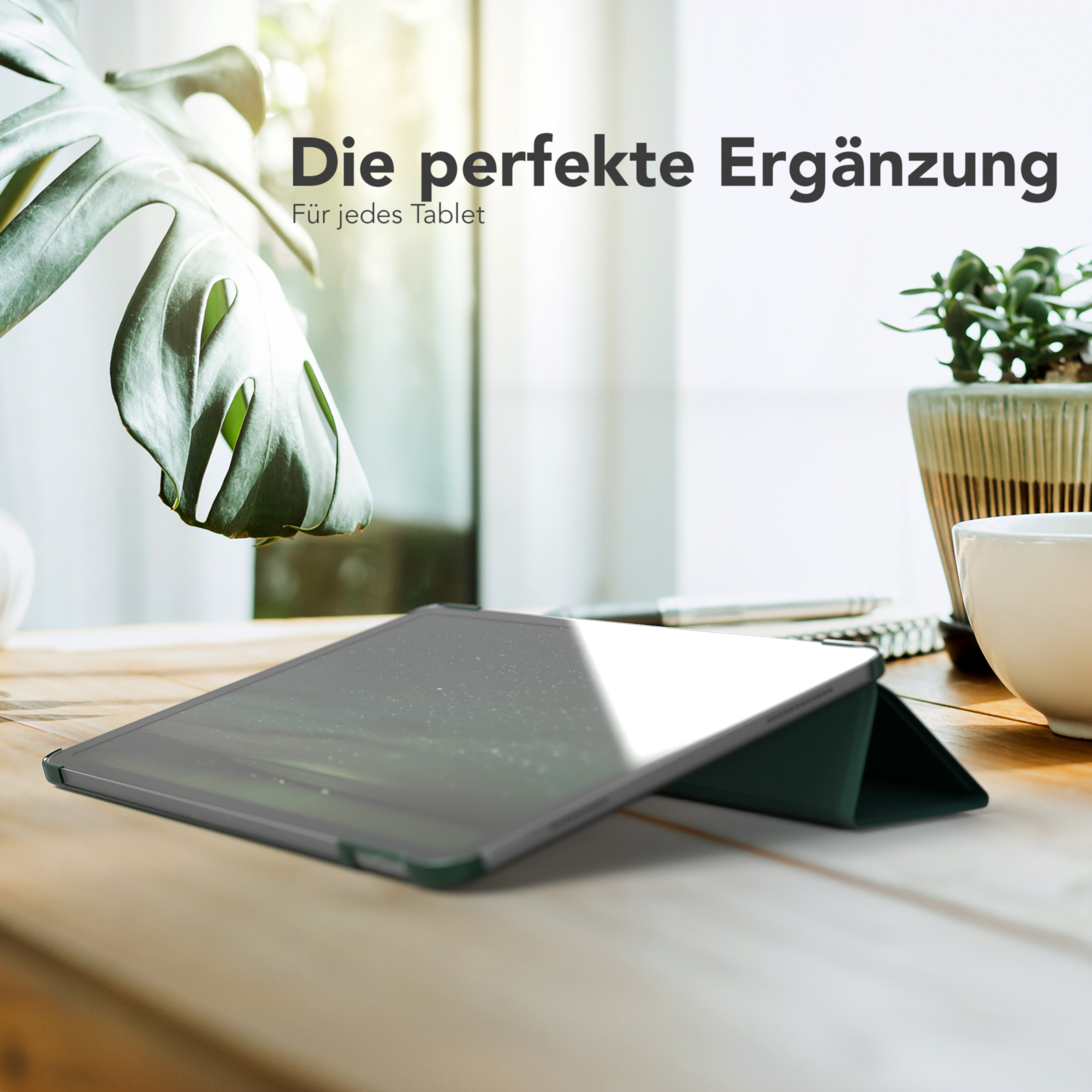 Tablet in grünem Case, auf Holztisch, neben Pflanze und Tasse, natürliches Licht.