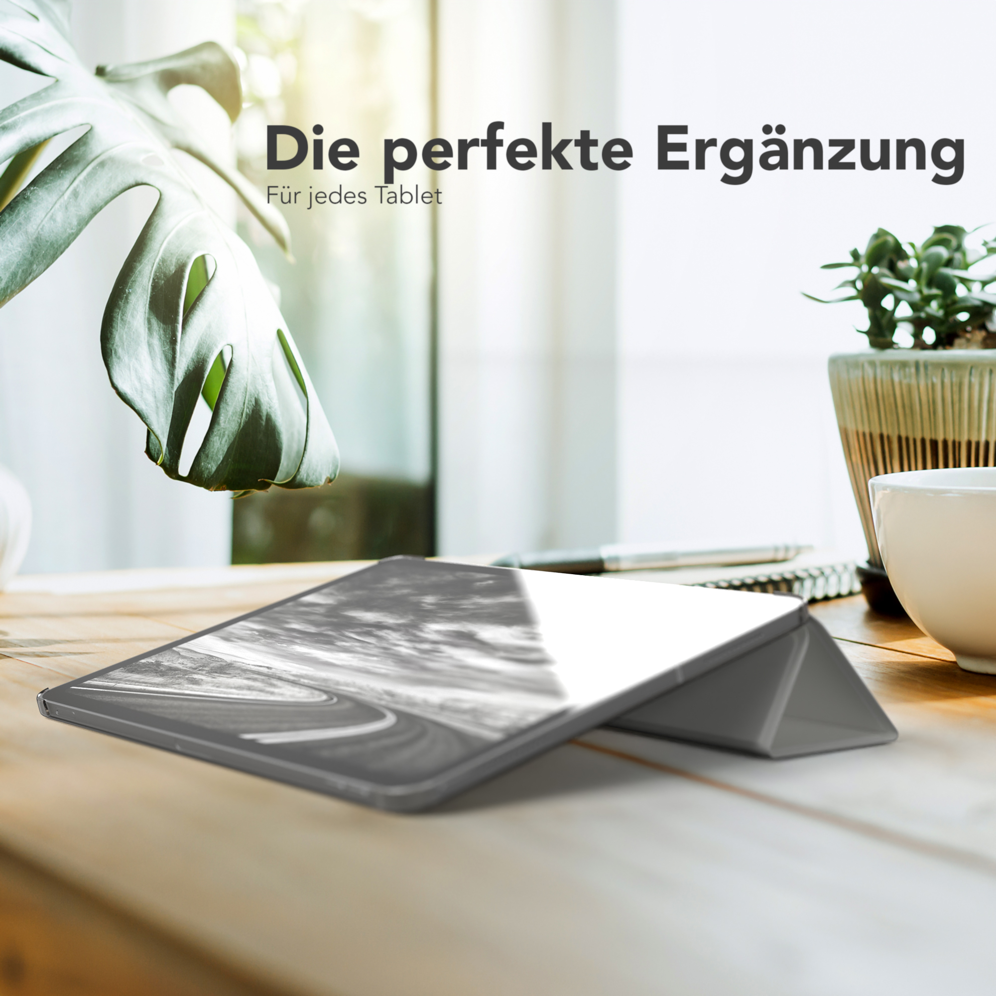 Tablet-Hülle, offen auf Holztisch mit Pflanze und Tasse. Hülle grau. Text: Die perfekte Ergänzung.