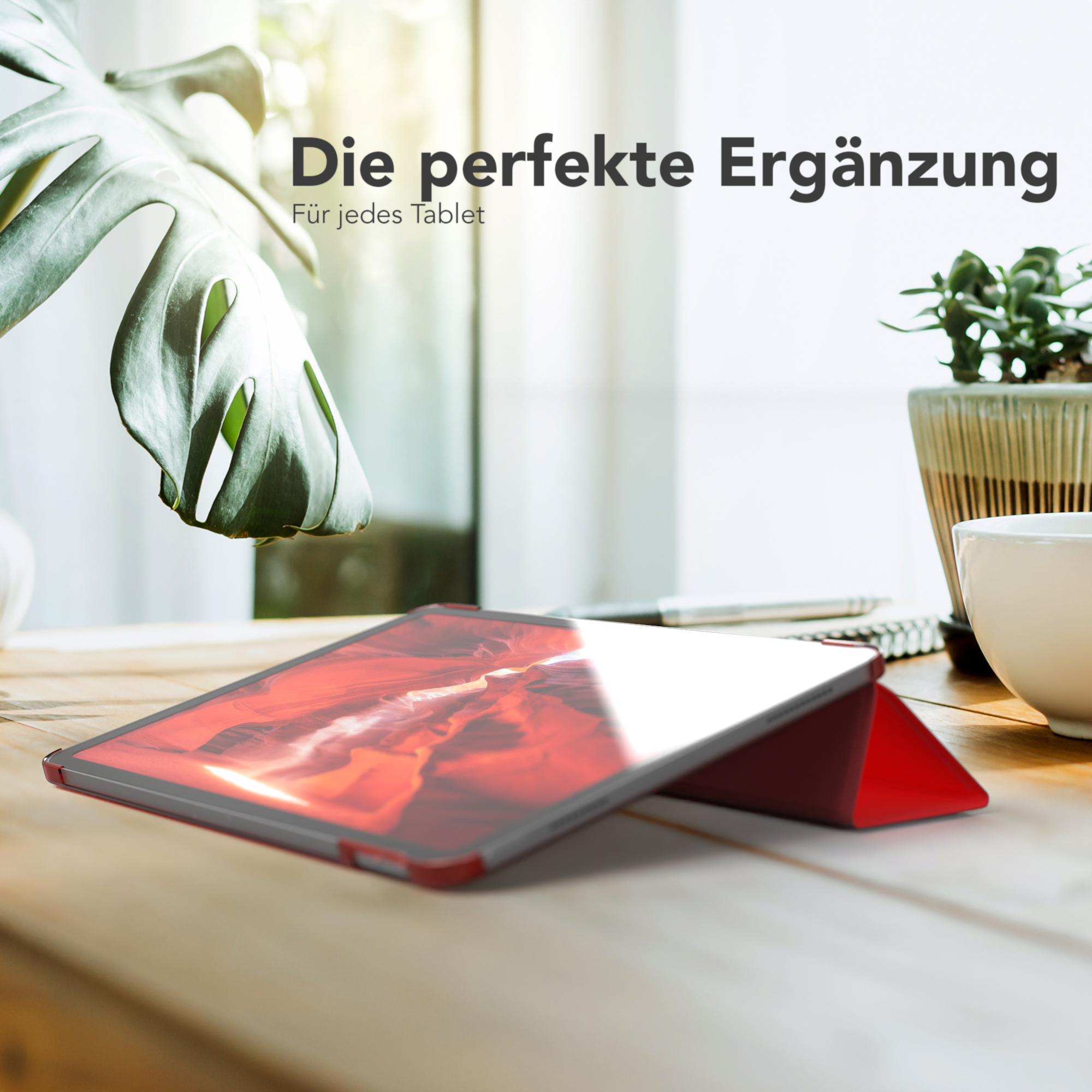 Tablet auf einem Holztisch mit roter Hülle, mit Pflanze und Kaffeetasse im Hintergrund.