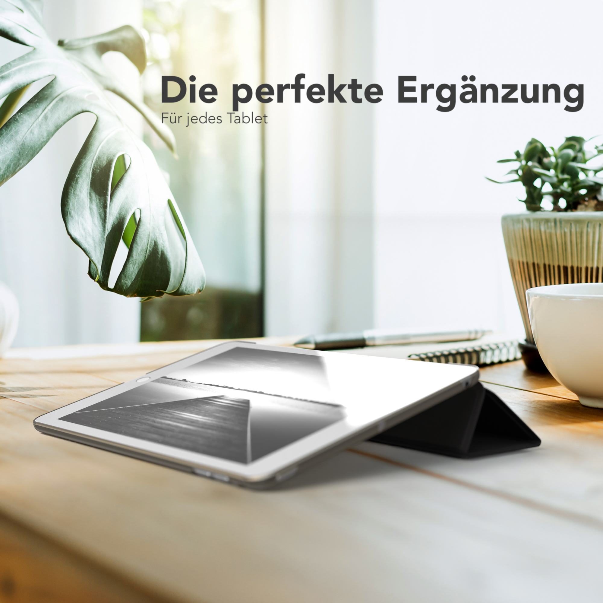 Ein Tablet in einer Hülle liegt auf einem Holztisch, mit einer Pflanze und einer Kaffeetasse im Hintergrund.
