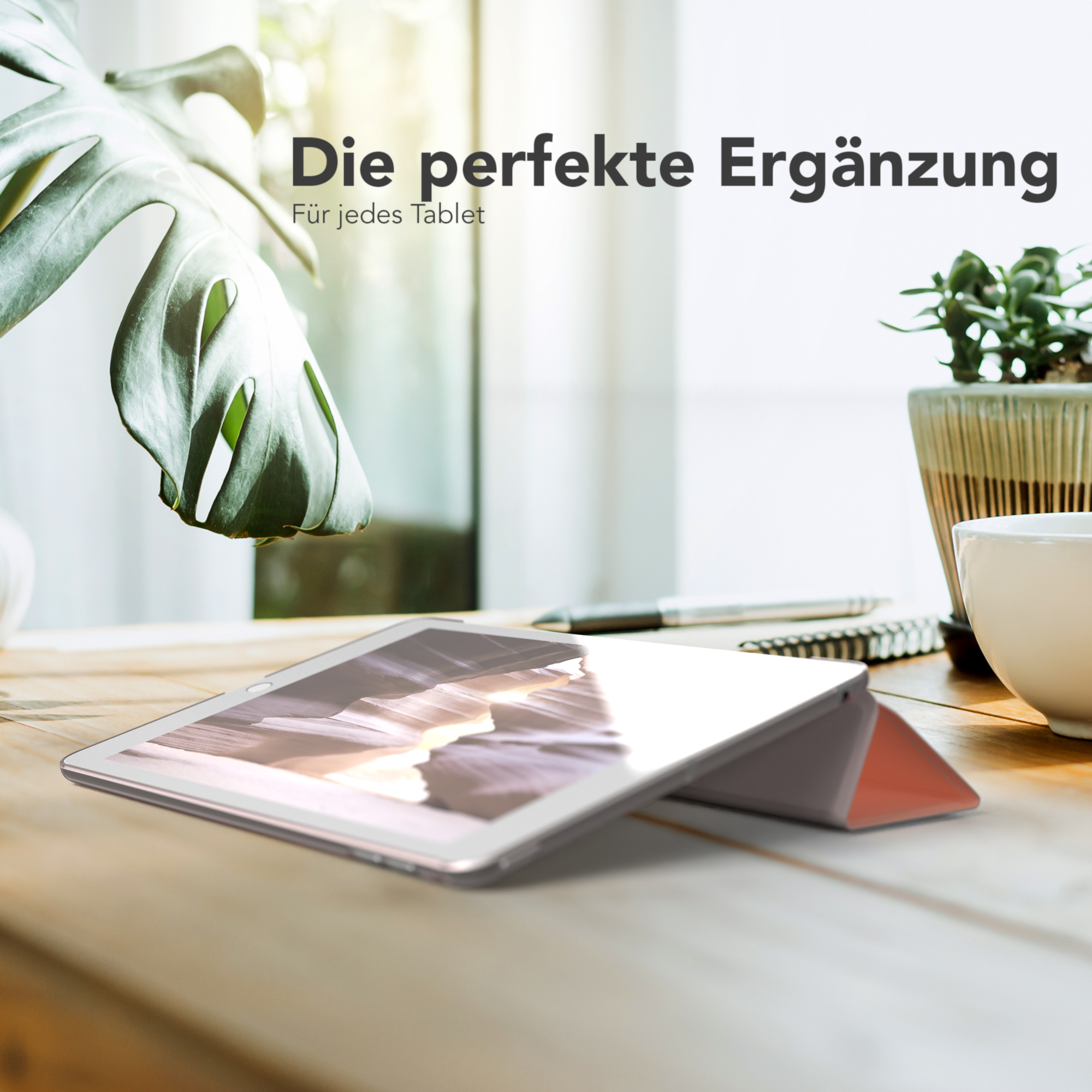 Ein Tablet in einer Hülle liegt auf einem Holztisch, mit einer Pflanze und einer Kaffeetasse im Hintergrund.