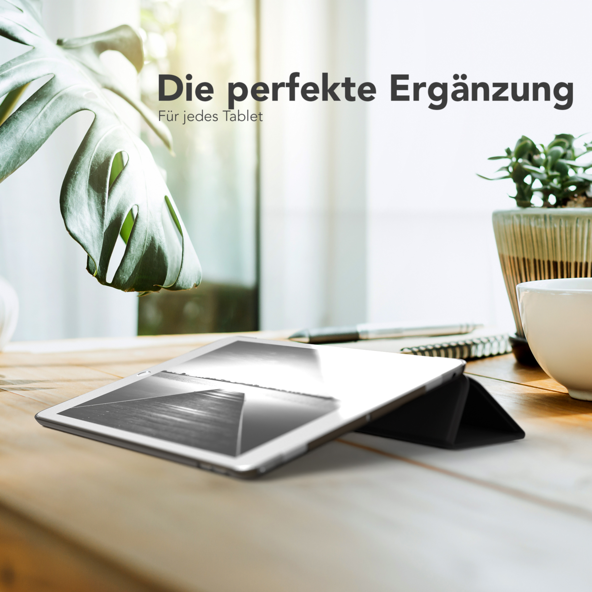 Ein Tablet mit Hülle auf einem Holztisch. Ein Blatt und eine Tasse sind im Hintergrund.