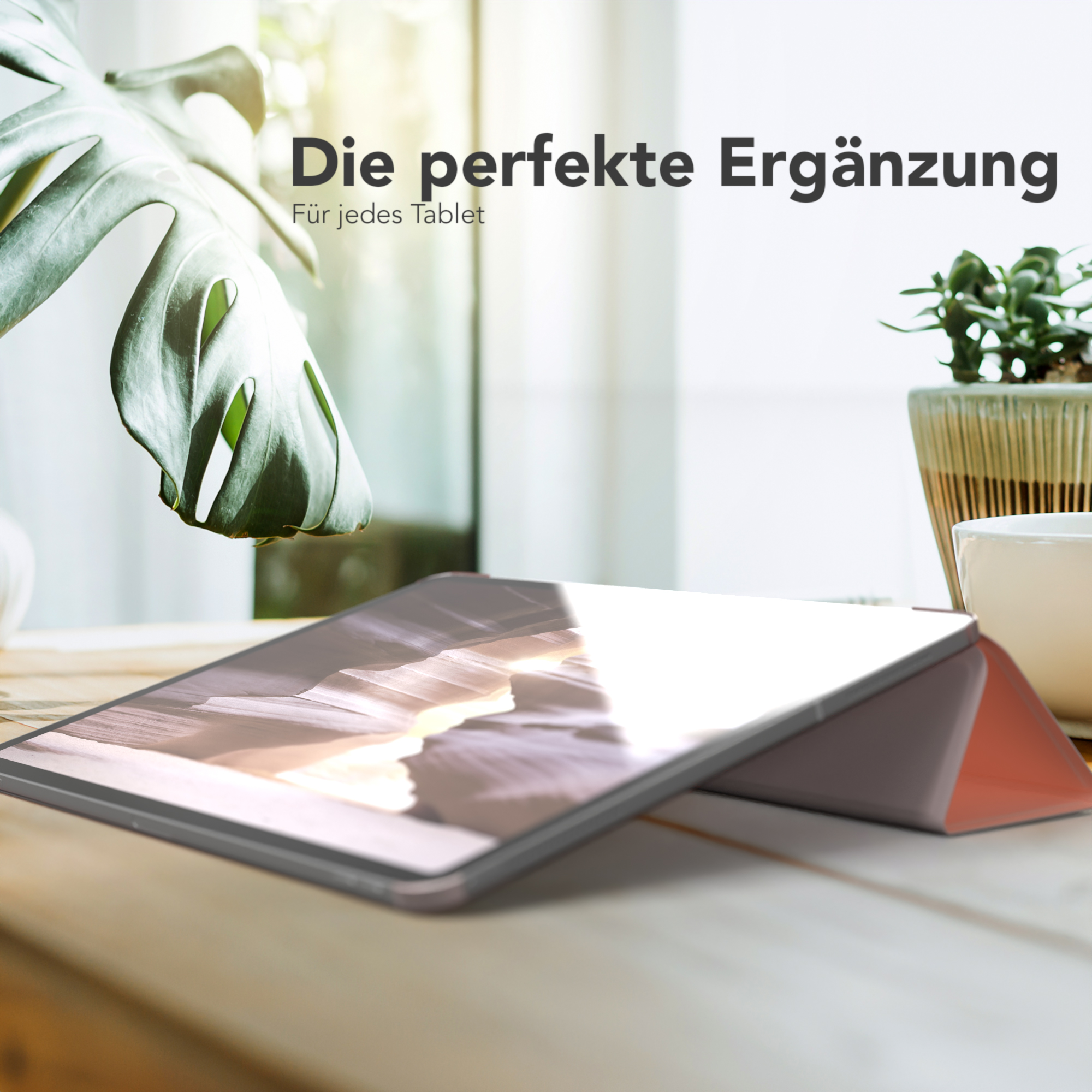Ein iPad liegt auf einem Holztisch mit einem Blatt und einer Topfpflanze, beleuchtet von Sonnenlicht.