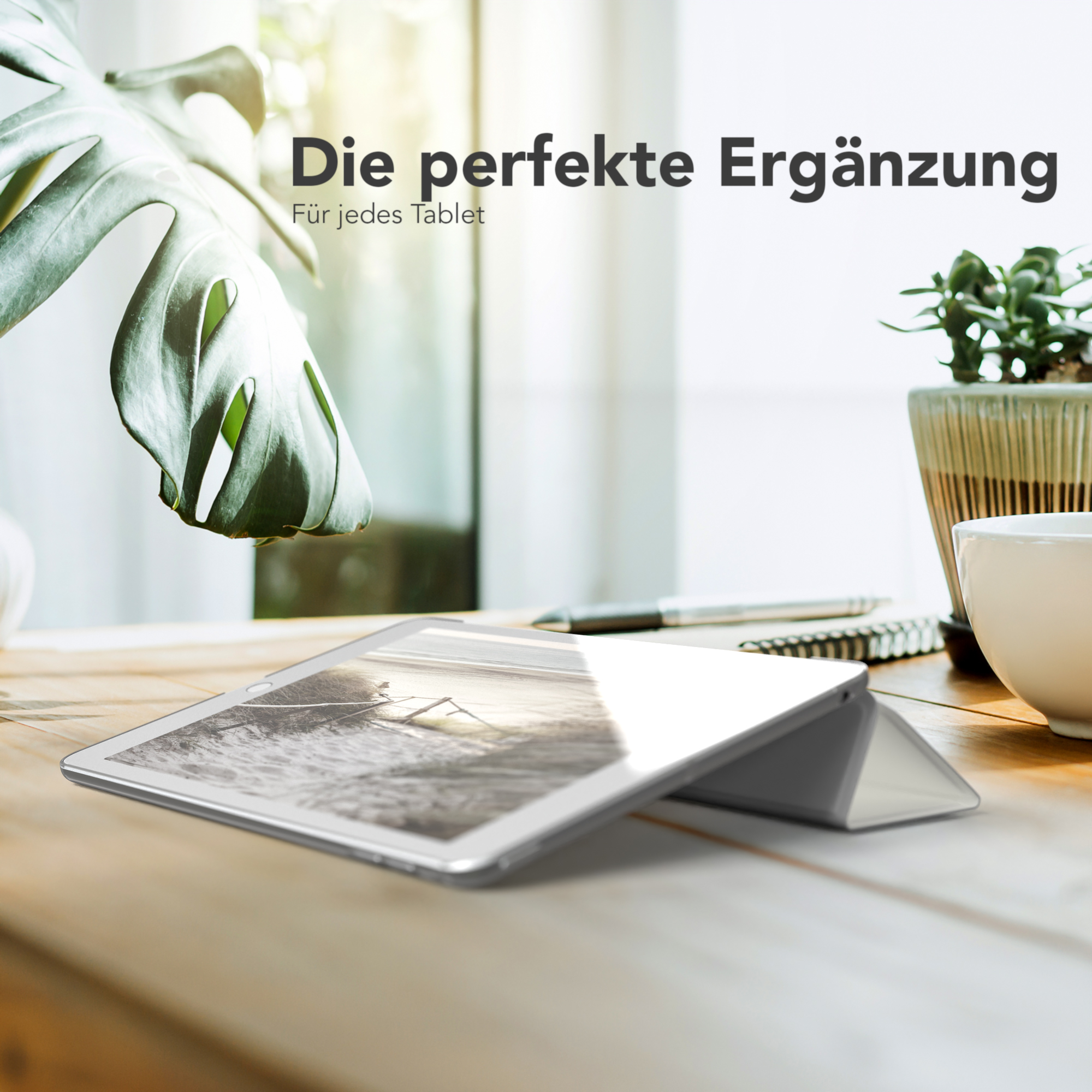 Ein Tablet auf einem Holztisch mit Hülle, neben einer Pflanze und einer Tasse. Die Szene ist beleuchtet.