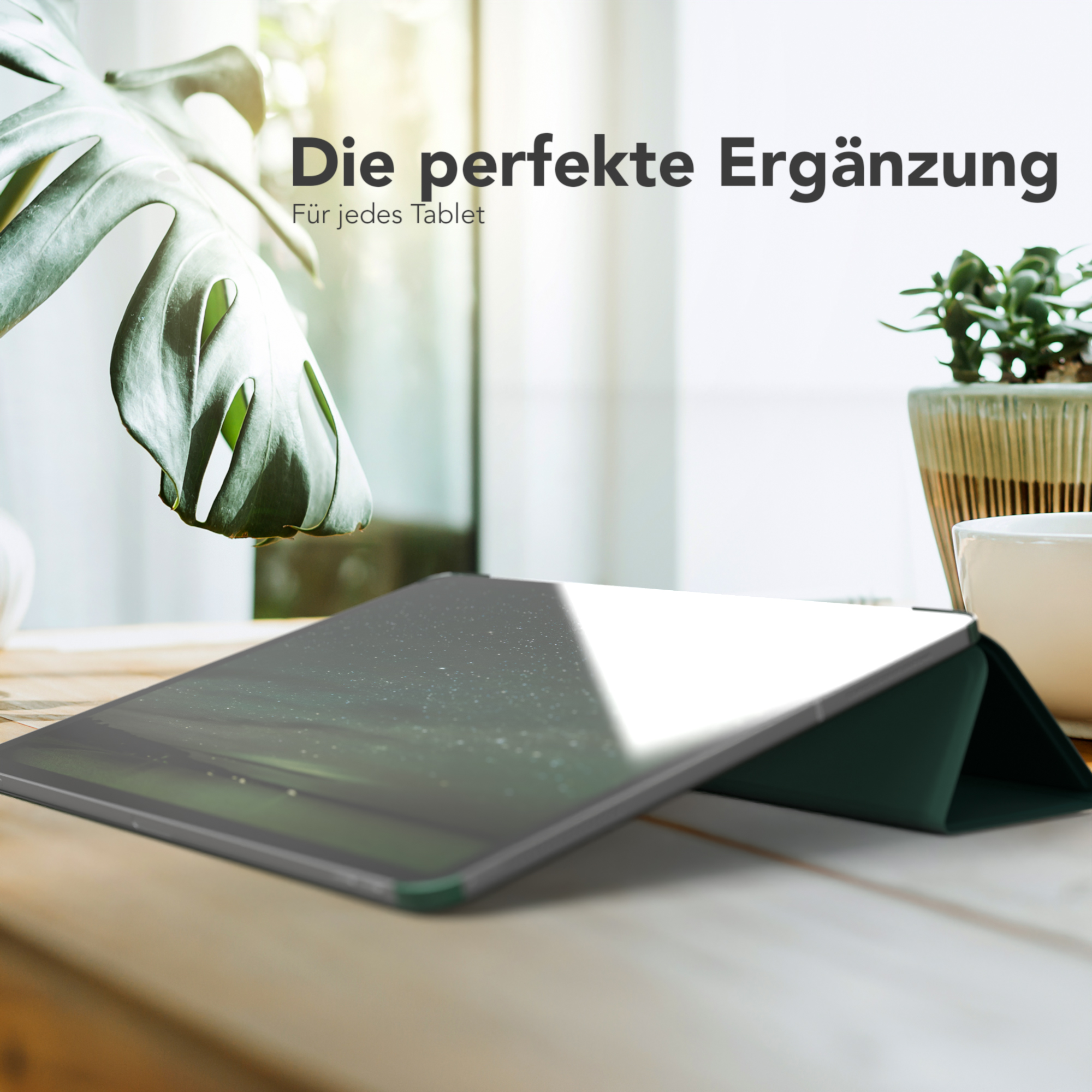 Tablet mit grüner Hülle liegt auf einem Holztisch. Eine Pflanze und ein Fenster sind im Hintergrund.