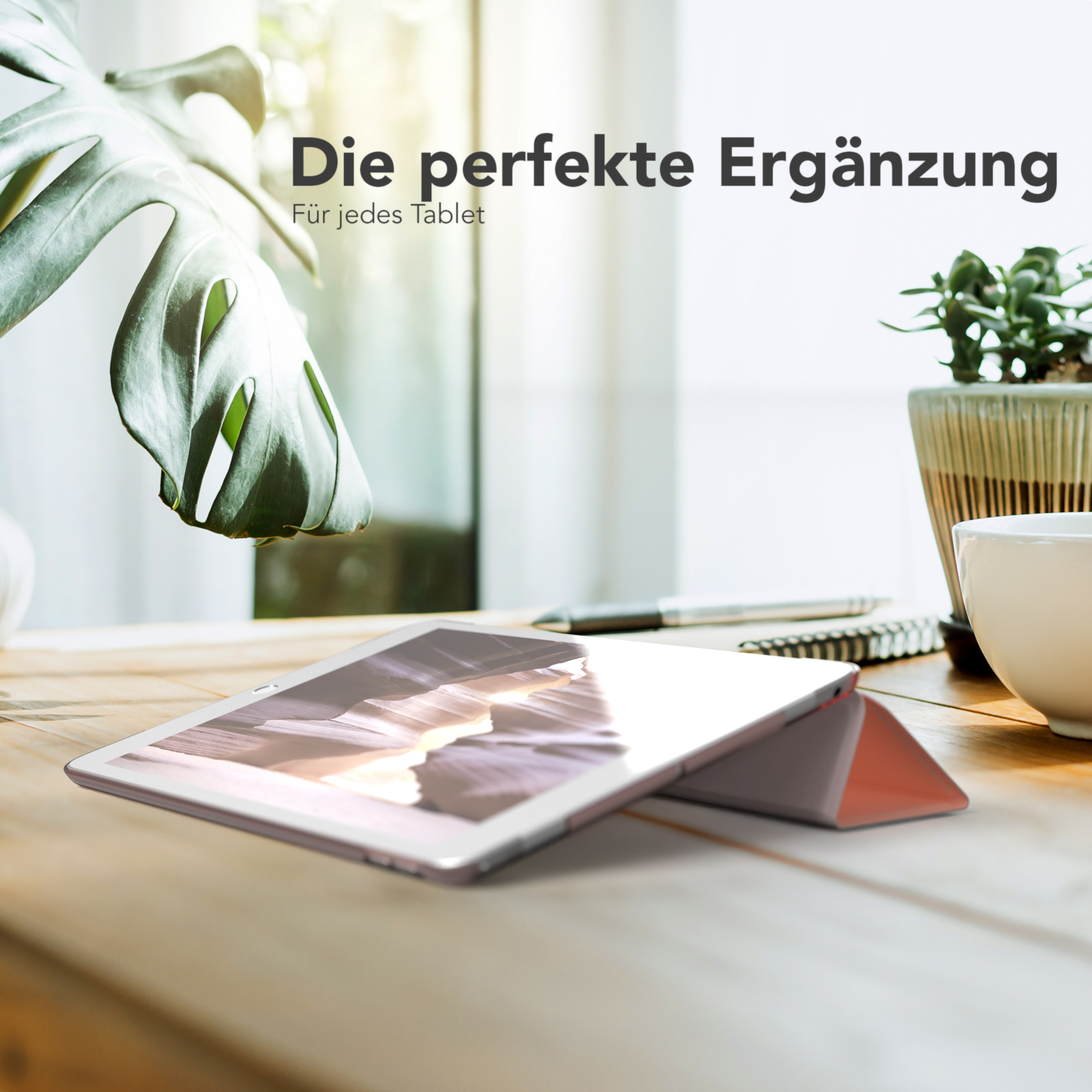 Ein Tablet auf Holzoberfläche mit rosa Cover und Pflanze im Hintergrund.