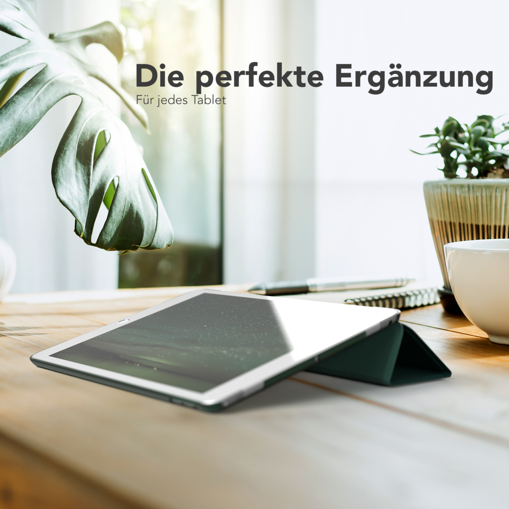 Ein Tablet auf einem Holztisch mit grüner Hülle, in der Nähe einer Pflanze und einer Kaffeetasse.