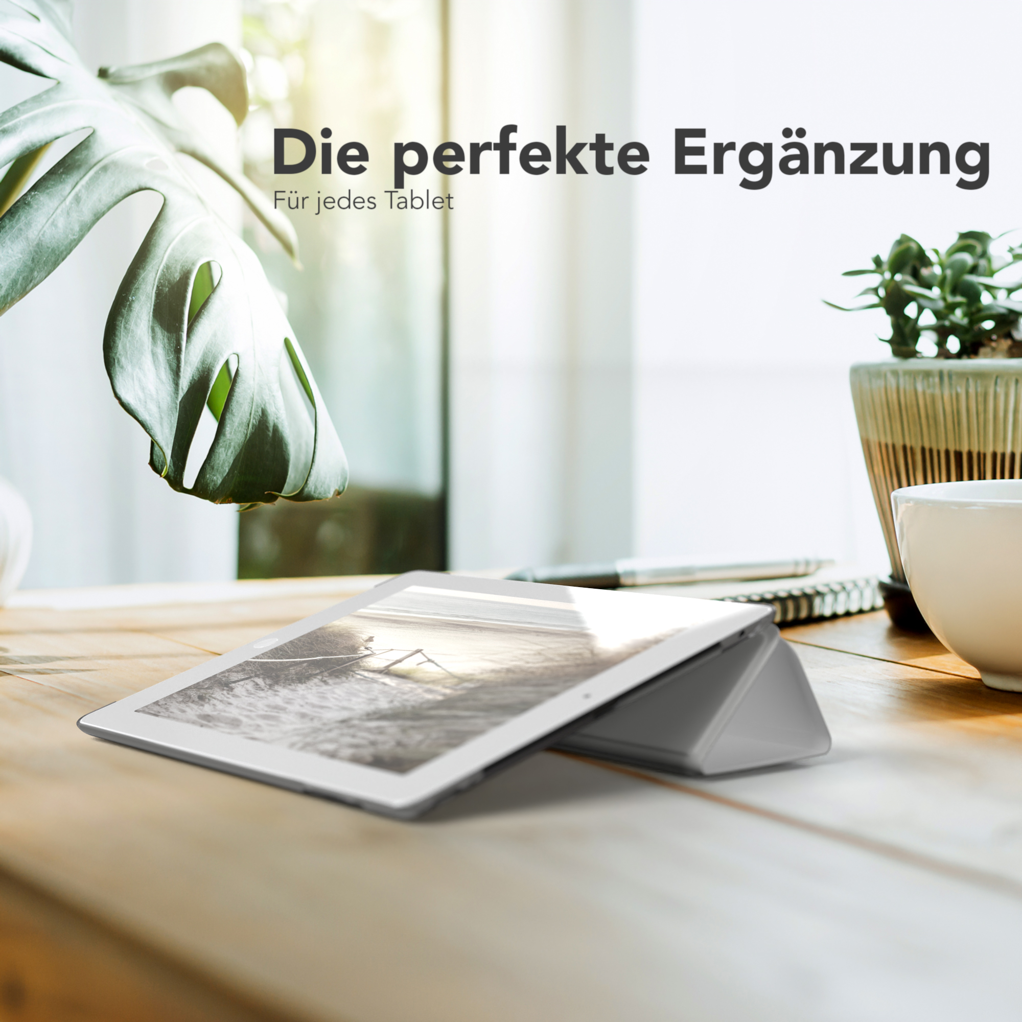 Tablet auf Holztisch, Pflanze im Topf, Fensterhintergrund und ein Stift.
