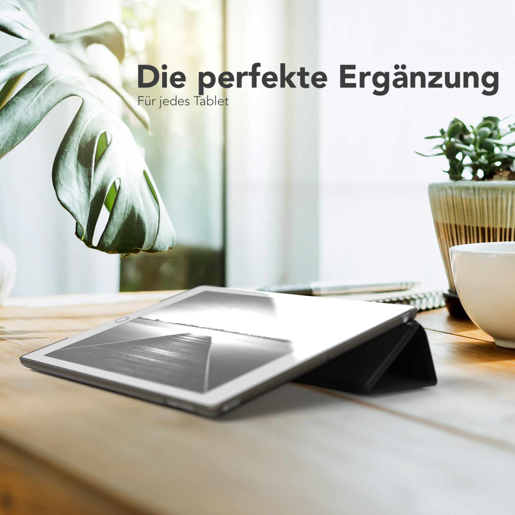 Ein Tablet auf einem Holztisch mit einer schwarzen Hülle und einer Pflanze.