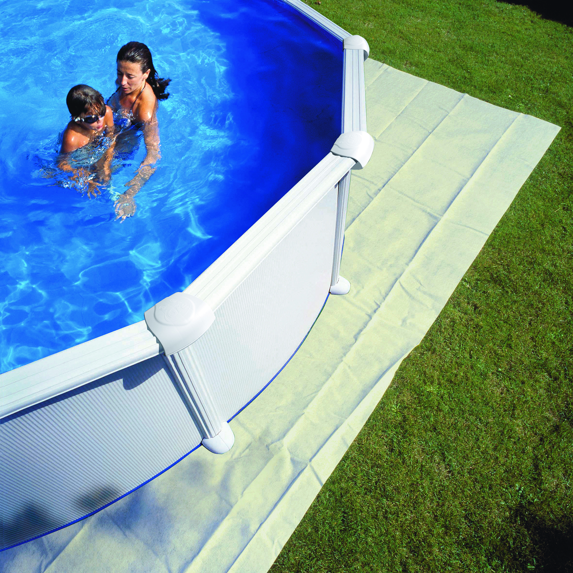 Zwei Personen in einem Pool, umgeben von einem weißen Rand und grünem Gras.