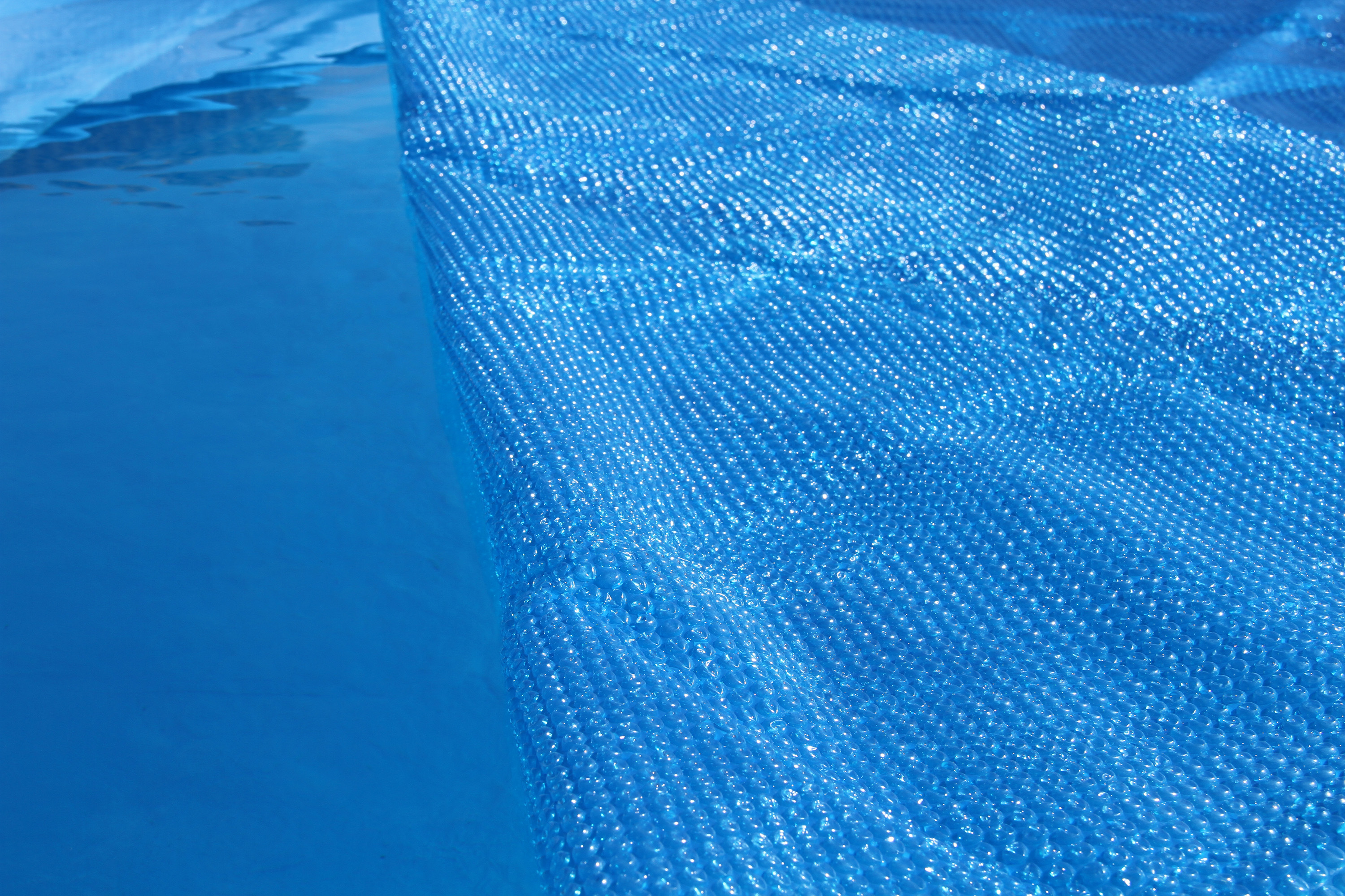 Blaues Poolwasser, bedeckt von einer blauen, blasenstrukturierten Schutzabdeckung.