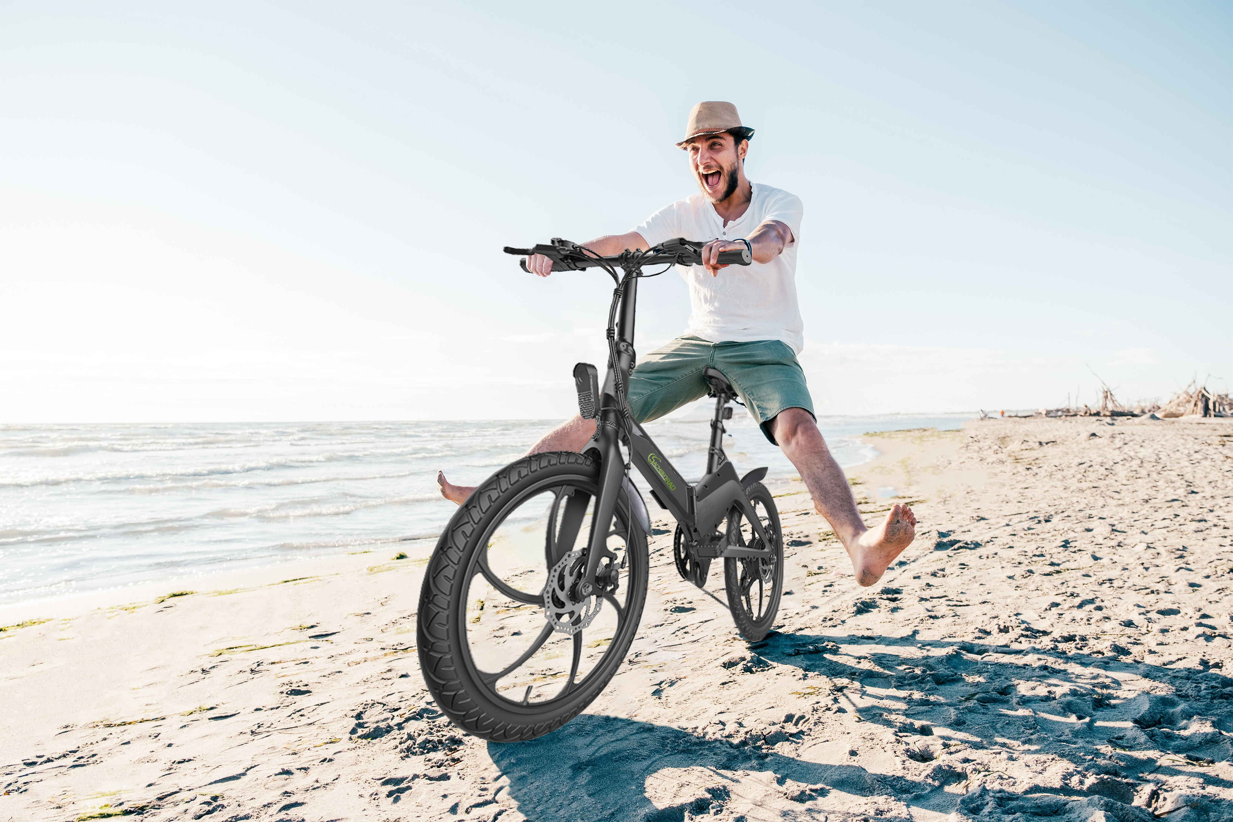 Mann fährt E-Bike am Strand. Er ist barfuß und lächelt vor Freude.