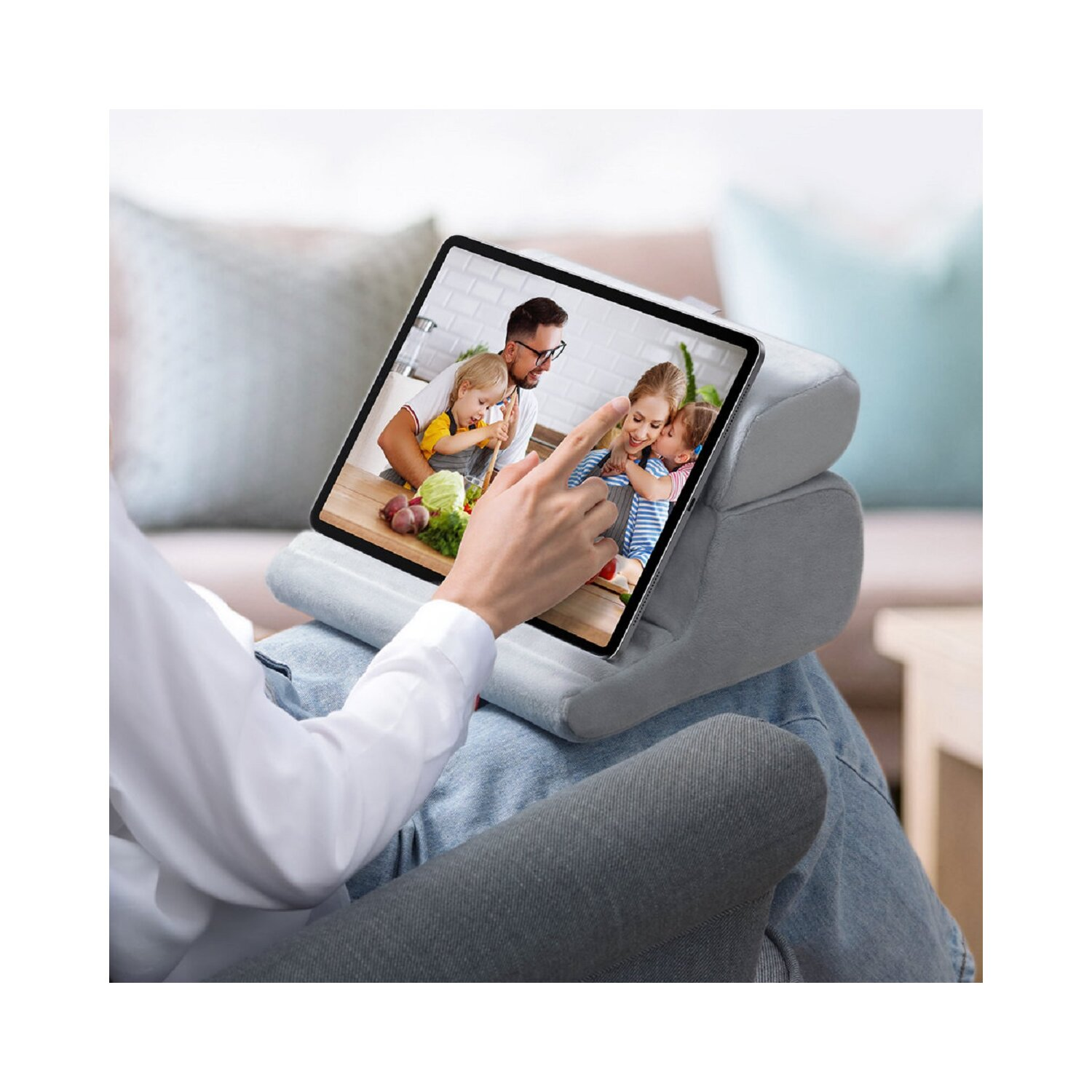 Osoba trzyma tablet oparty na poduszce, pokazujący film z rodziną. Kanapa w tle.