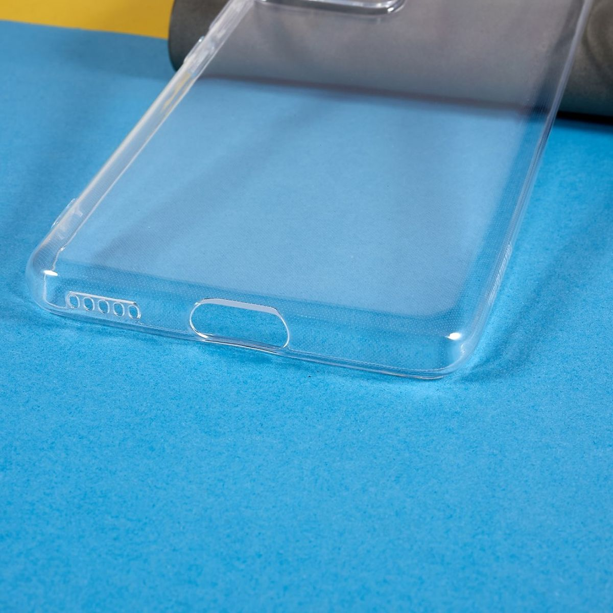Eine durchsichtige Handyhülle liegt auf einem blau-gelben Hintergrund. Die Hülle hat Aussparungen.