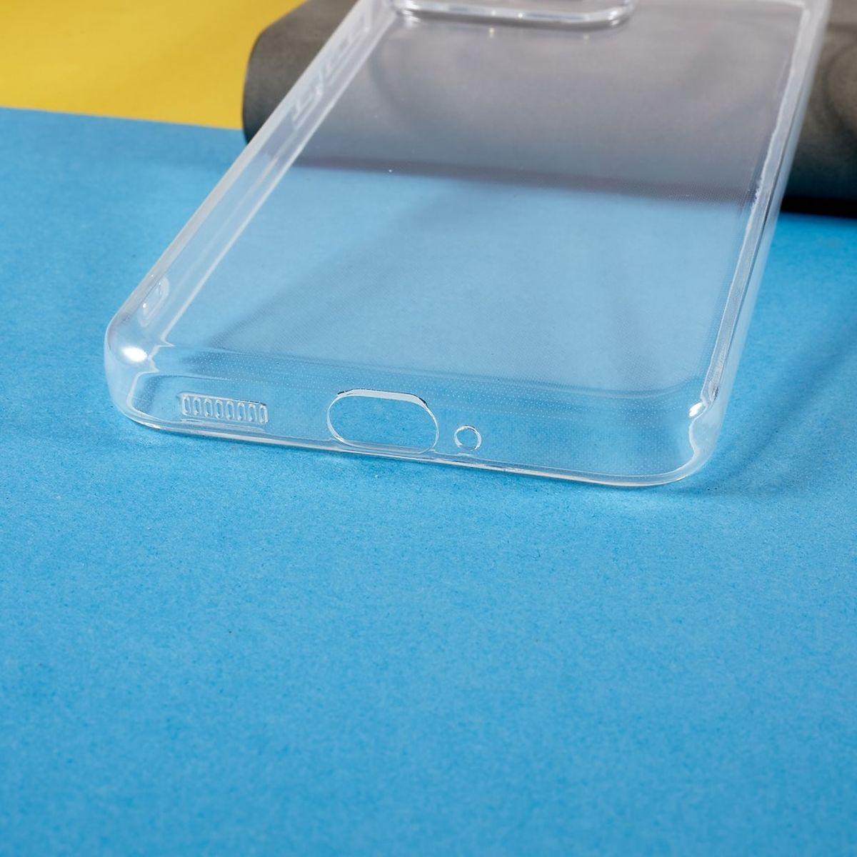 Transparente Handyhülle auf blau-gelbem Hintergrund. Hülle hat Kamera- und Anschlussausschnitte.
