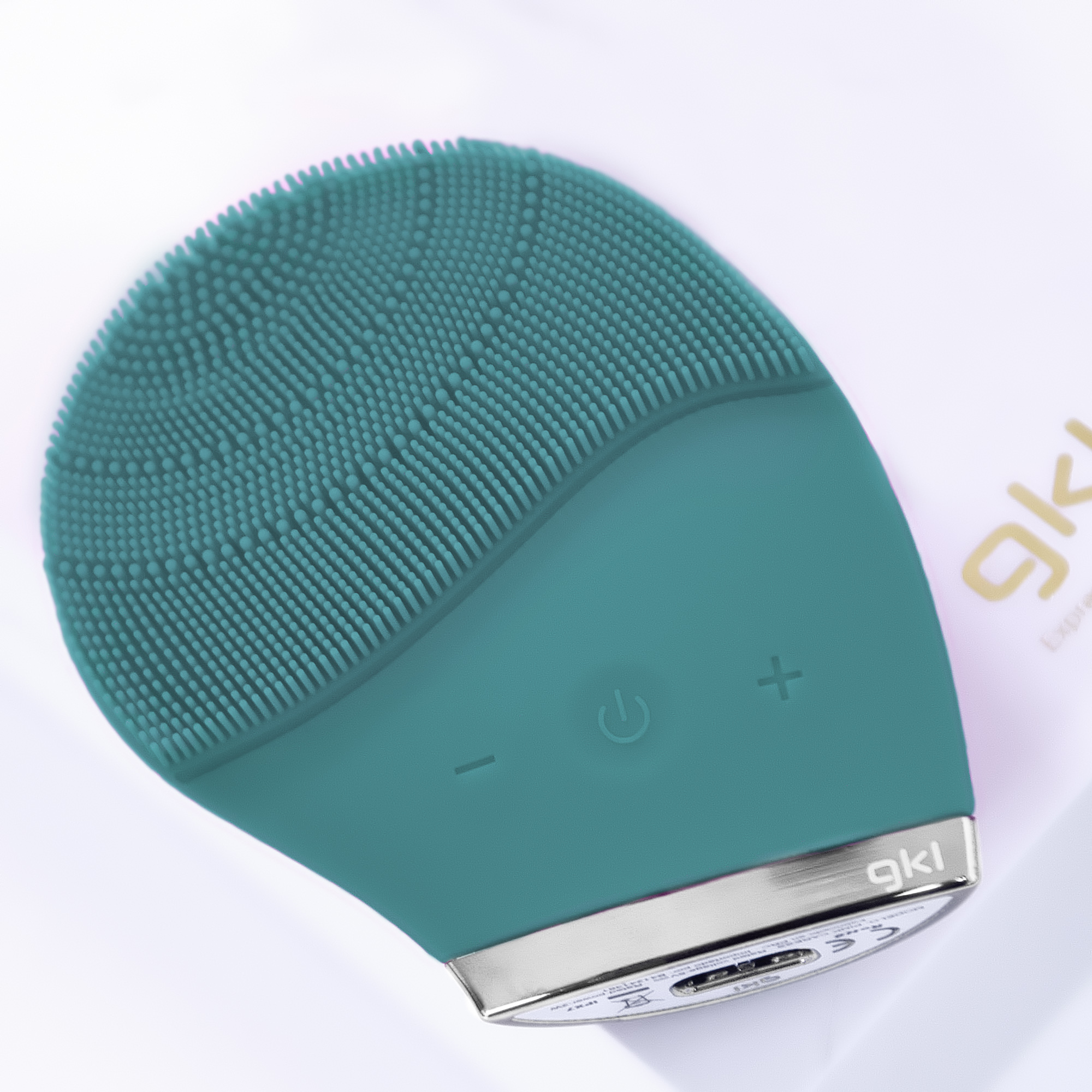 Un cepillo de limpieza facial de color verde azulado sobre una superficie blanca, con botones y controles.