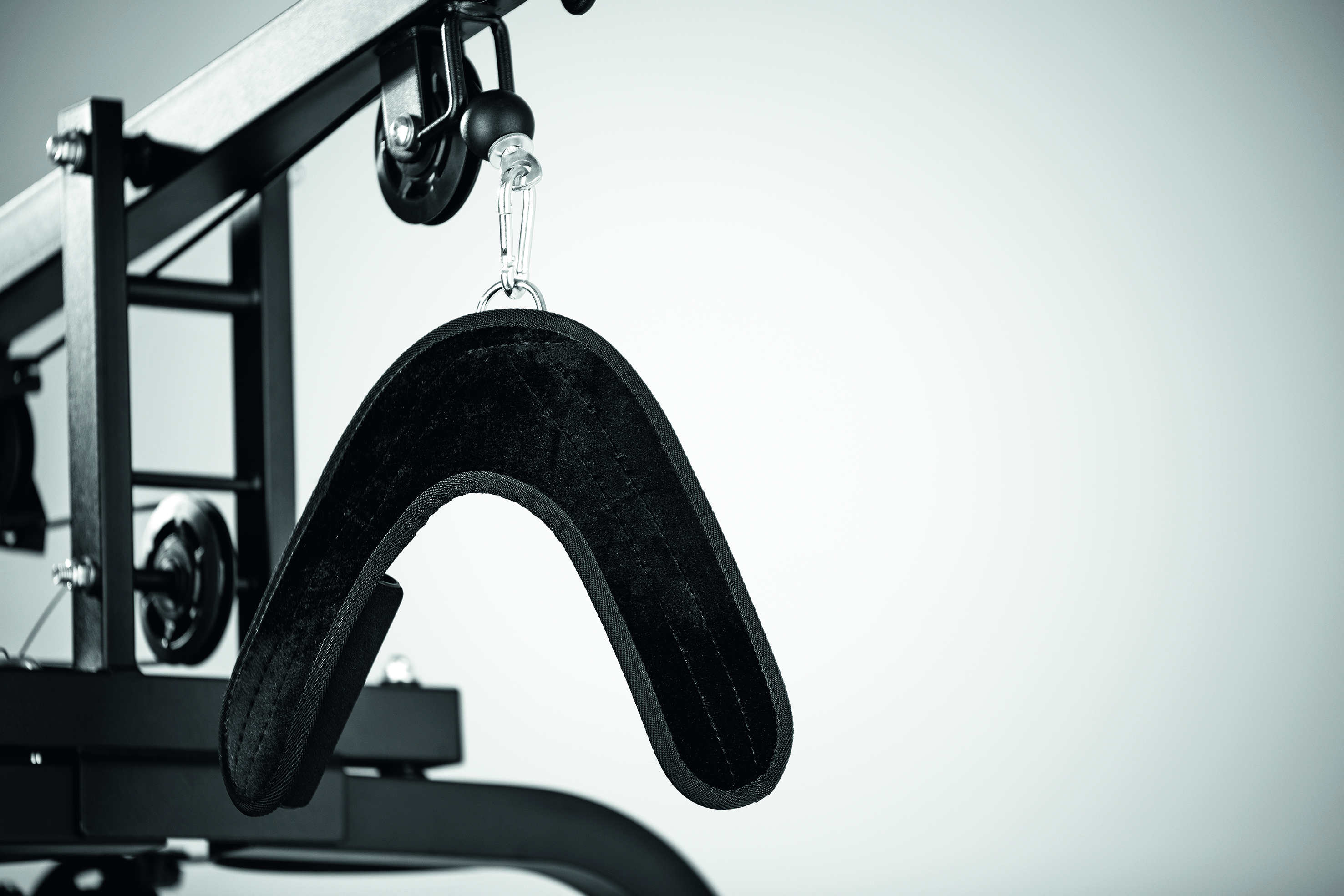 Ein schwarzer Nackenstützaufsatz für ein Fitnessgerät. Er hängt an einer Metallkonstruktion.