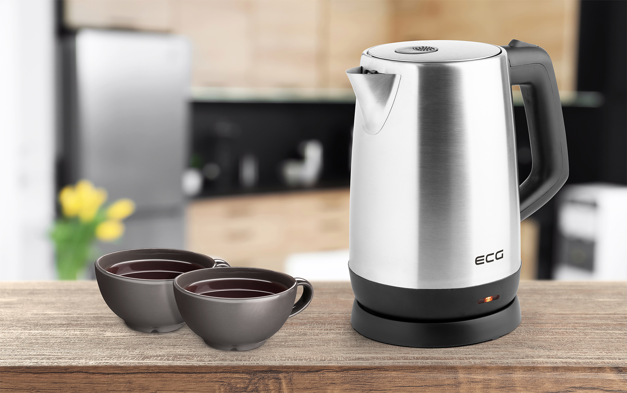 Srebrny czajnik elektryczny z dwoma ciemnoszarymi filiżankami na drewnianym stole. Rozmyte tło.