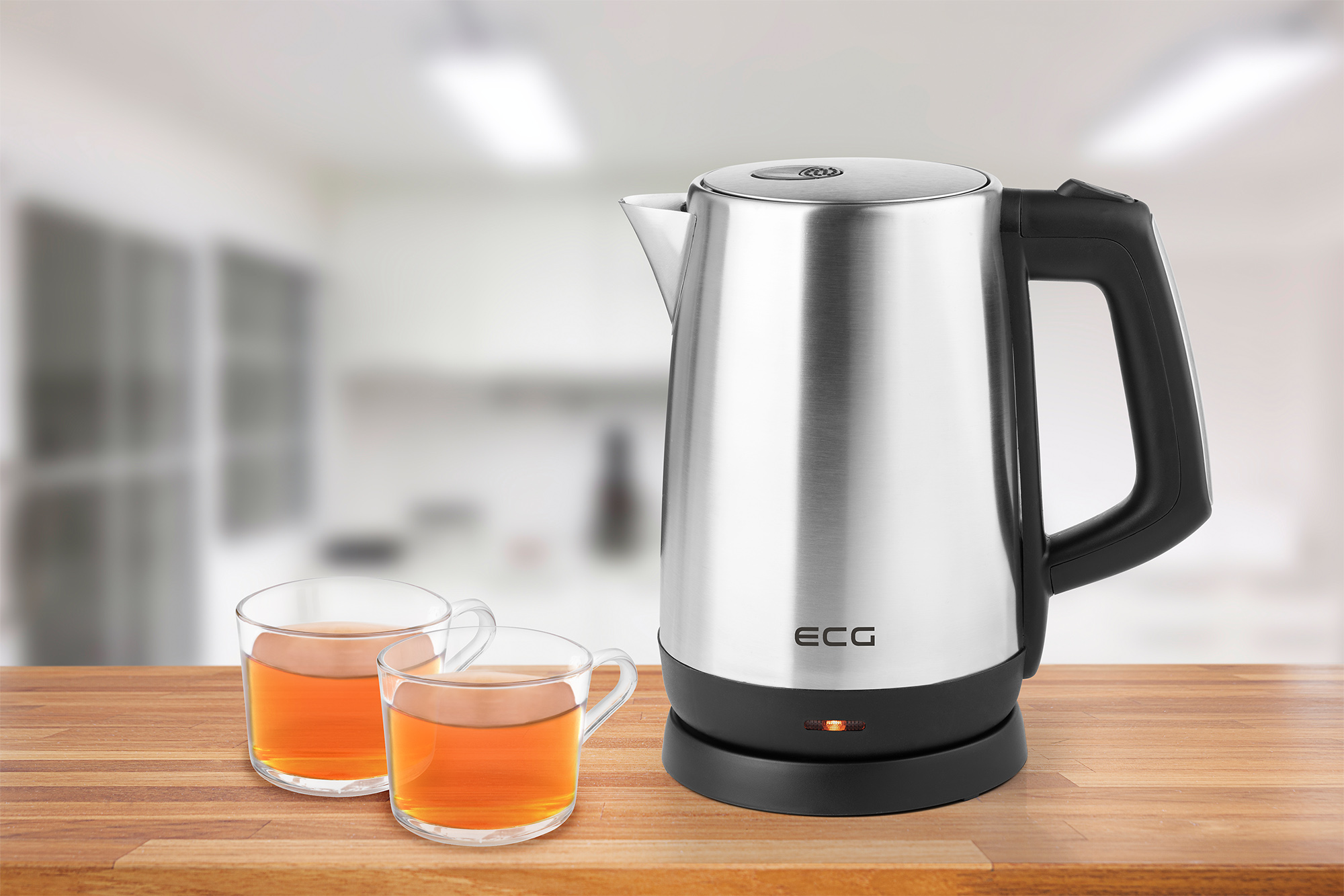Czajnik elektryczny na drewnianym stole. Dwie szklanki herbaty i rozmyte tło kuchni.