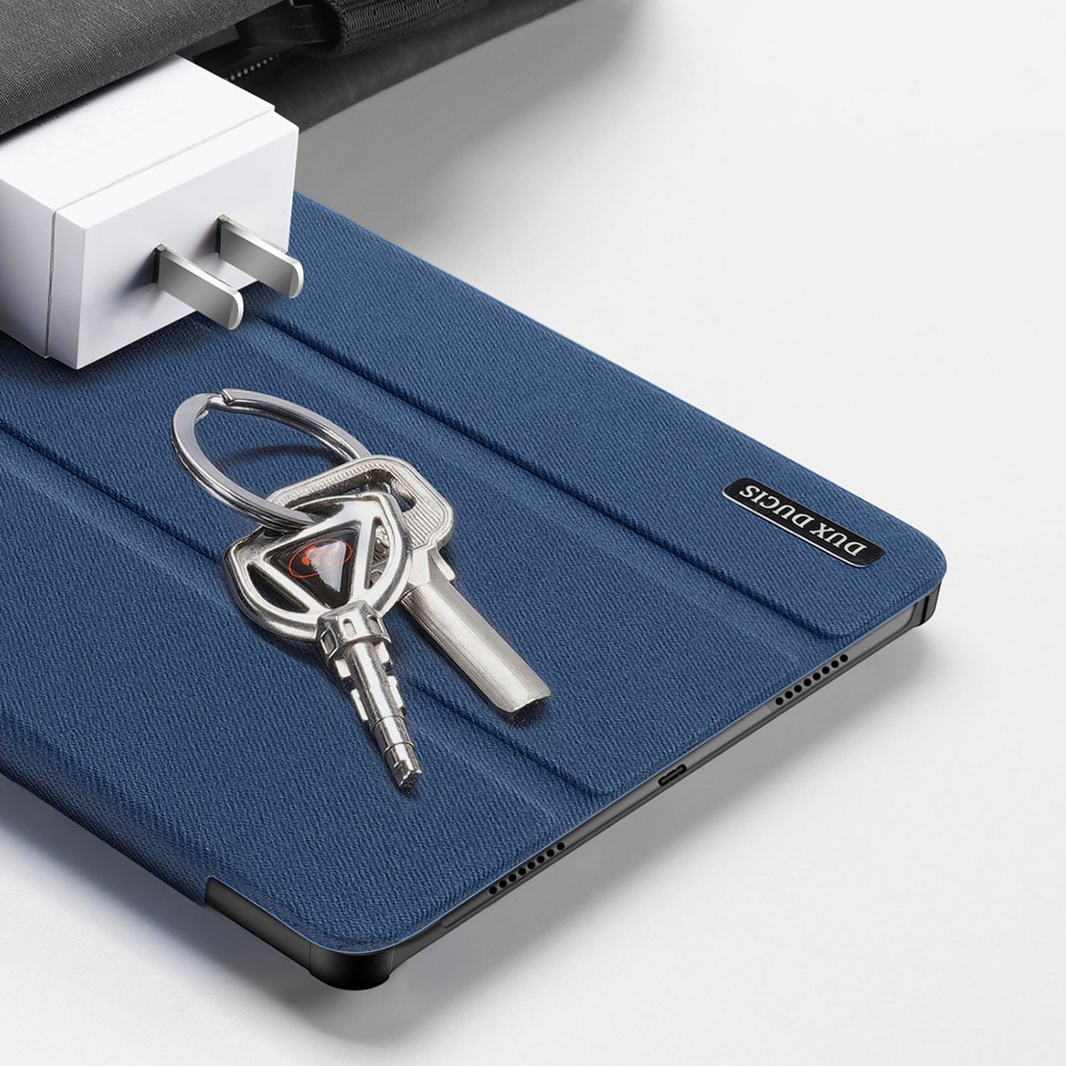 Ein Tablet in einer blauen Hülle mit Schlüsseln, einem Ladegerät und dem Markennamen auf einem Tisch.