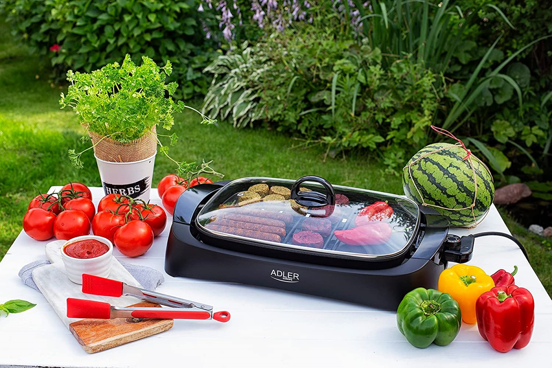 Ein Grill mit Gemüse und Essen auf einem weißen Tisch, umgeben von einem Garten.