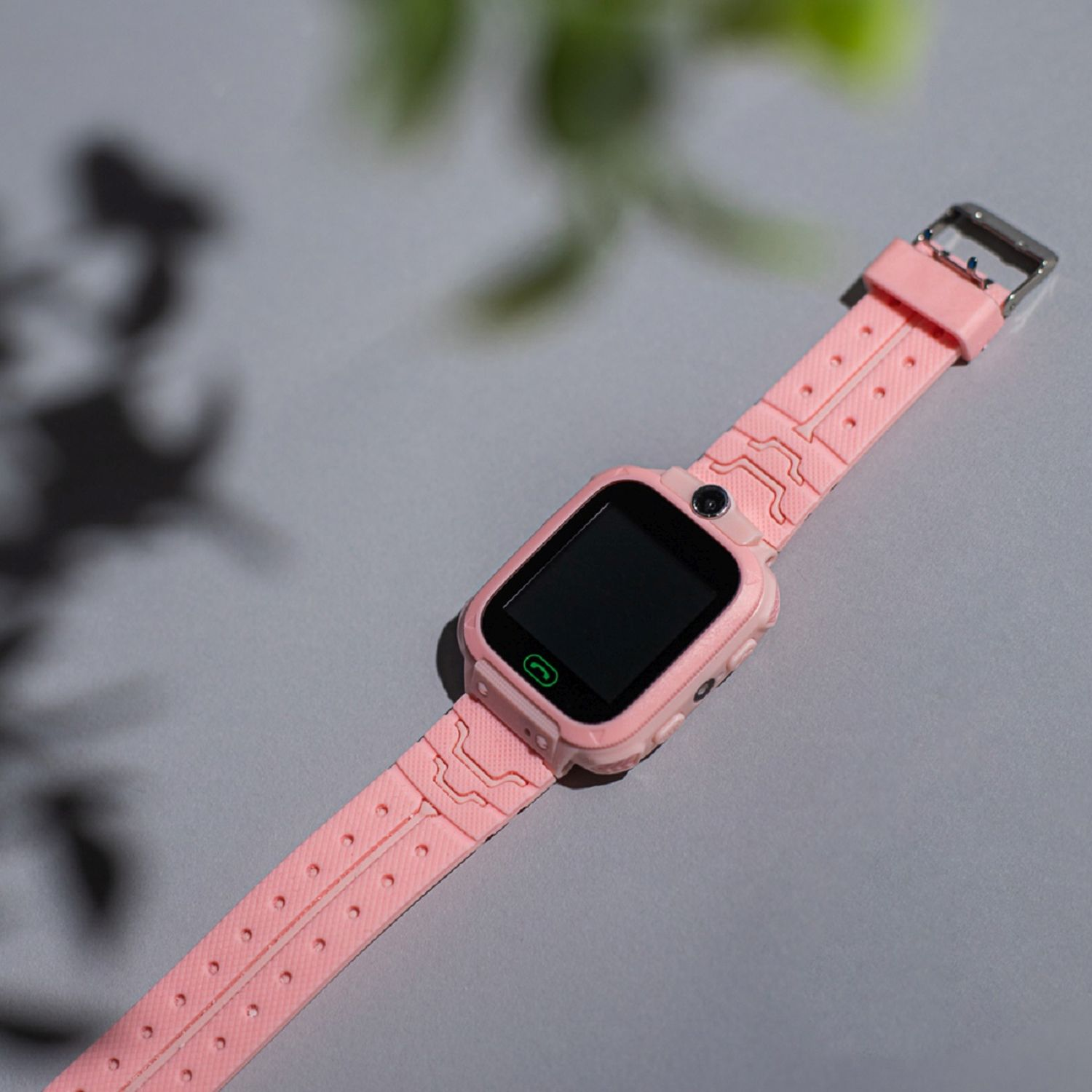 Rosa Smartwatch mit schwarzem Bildschirm, auf einer hellgrauen Oberfläche. Das Armband ist befestigt.