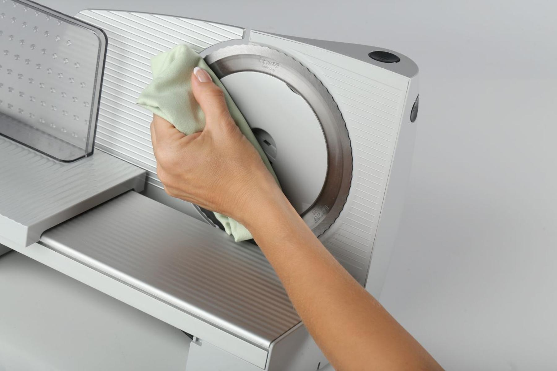 Osoba czyszcząca ostrze srebrnej krajalnicy do żywności zieloną szmatką. Białe tło.