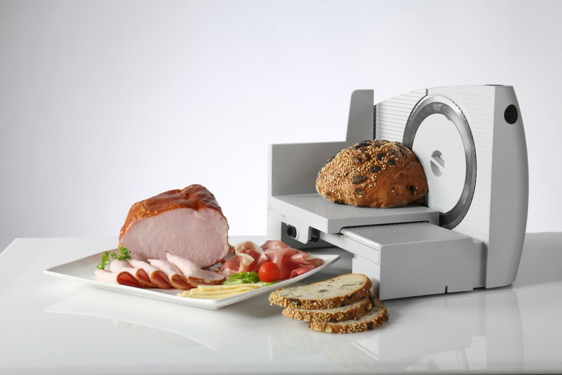 Krajalnica do mięsa z chlebem i mięsem na białej powierzchni. Scena jest dobrze oświetlona.