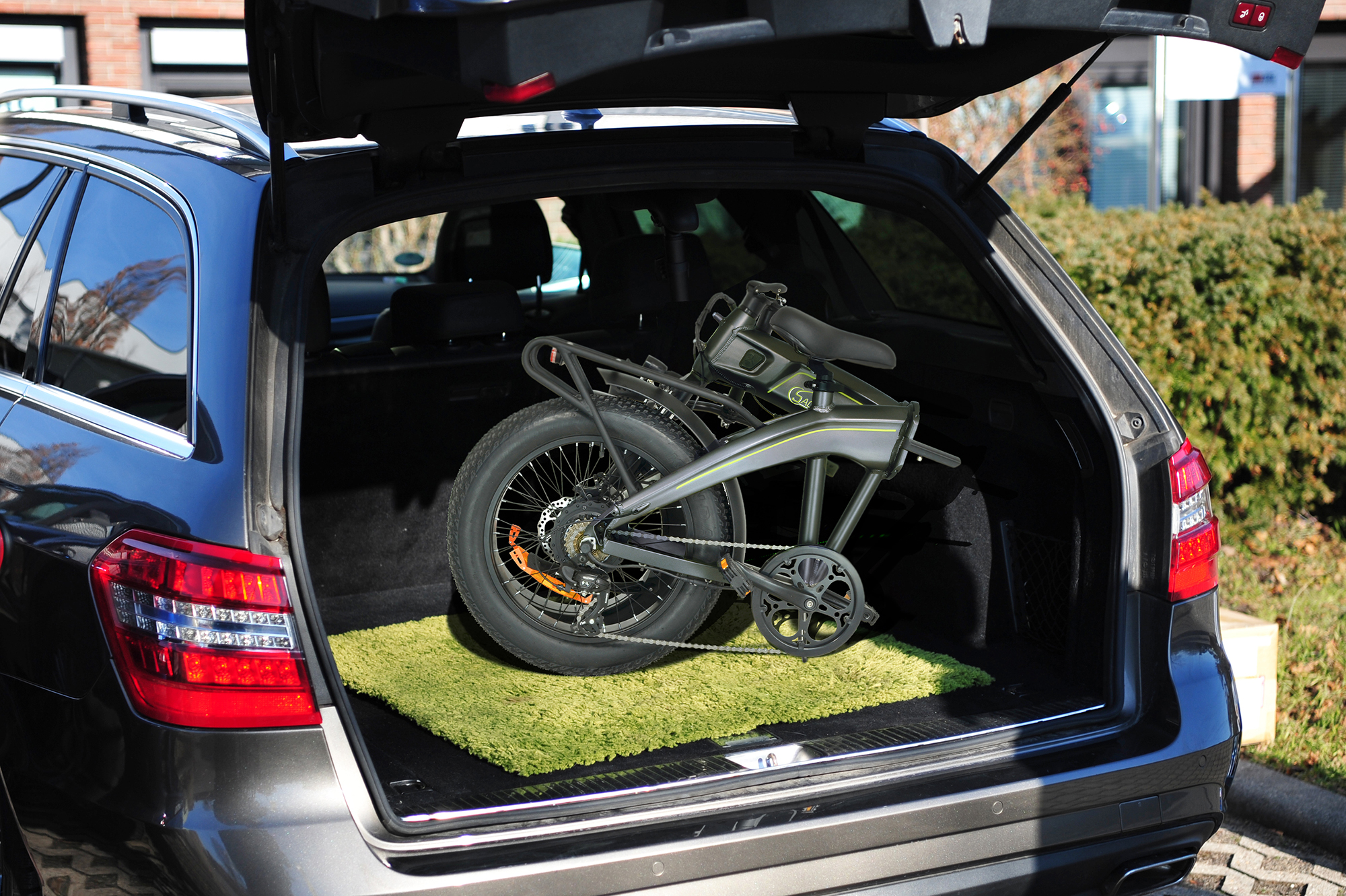 Ein gefaltetes schwarz-graues Fahrrad liegt im Kofferraum eines Autos auf einer grünen Matte.